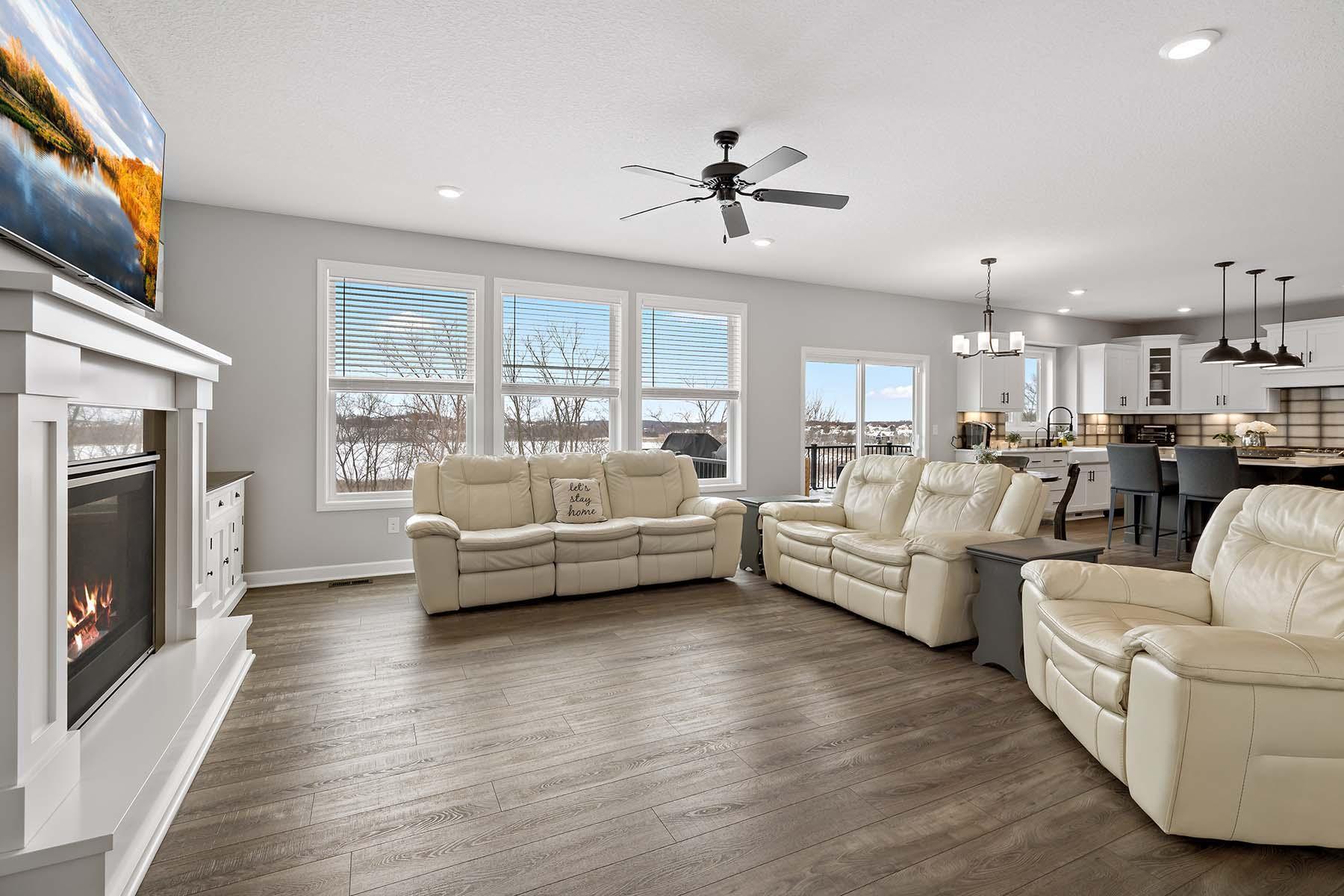 The living room is bright and inviting, highlighted by recessed lighting and wall-to-wall windows that showcase panoramic views of the backyard.