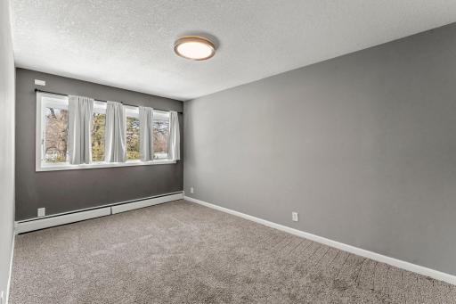 A view of the second bedroom, featuring new carpeting, a large window, and generous closet space with updated wire shelving.