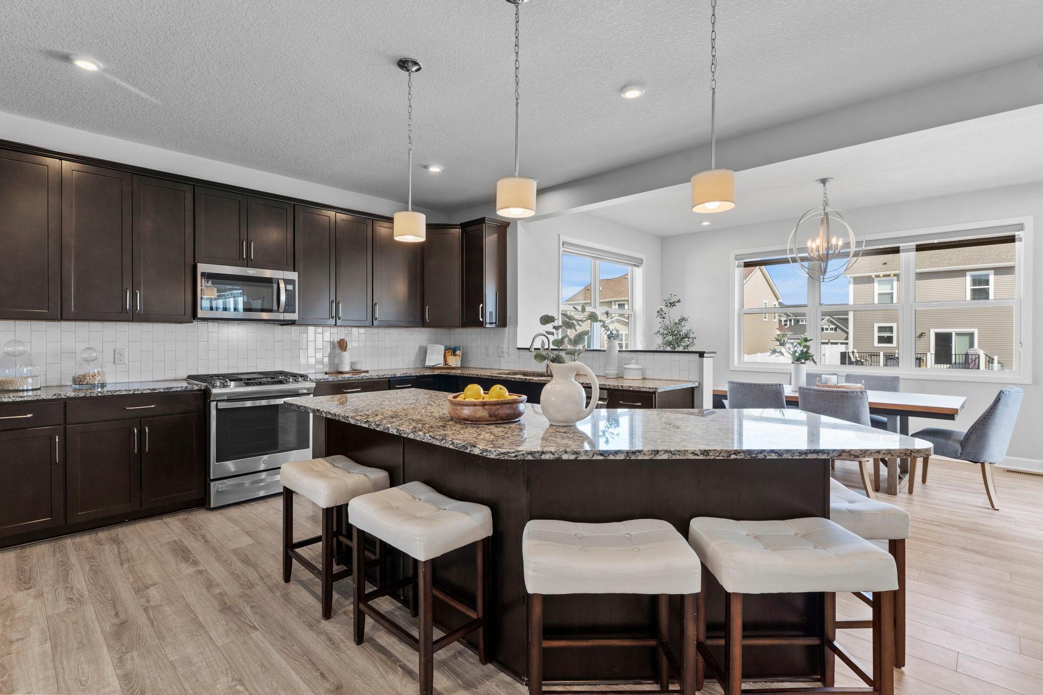This home’s kitchen is a chef’s dream, featuring abundant cabinetry, expansive granite countertops, and a large center island with breakfast bar seating and pendant lighting.