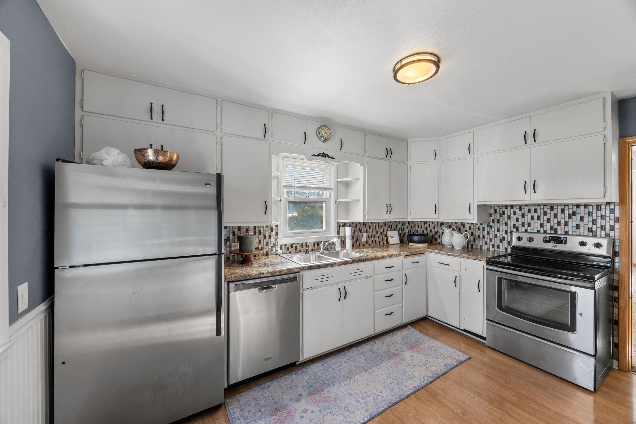 The kitchen features an eat-in dining area, stainless steel appliances, a tile backsplash, and a window overlooking the neighborhood.