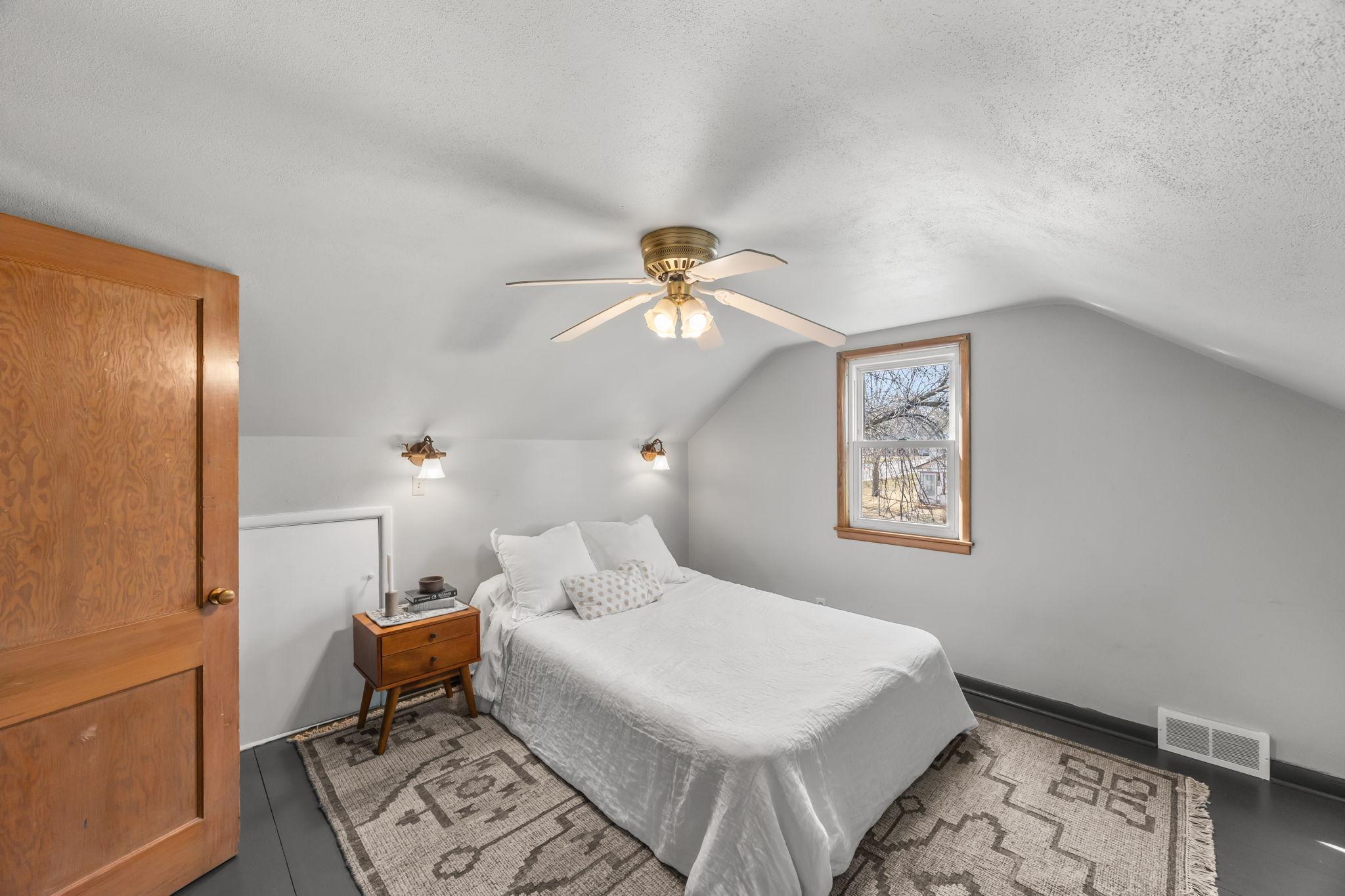 Primary bedroom suite complete with a ceiling fan, sconce lighting, closet, and convenient access to a lit crawl space for extra storage.