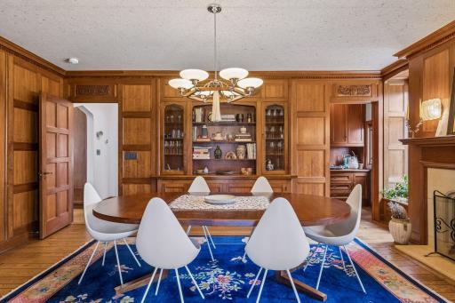 The formal dining room is accessible from a central hall or the sunroom and features rich mahogany raised panel walls, built-in cabinetry and service area, a wood-burning fireplace, and separate bar area.