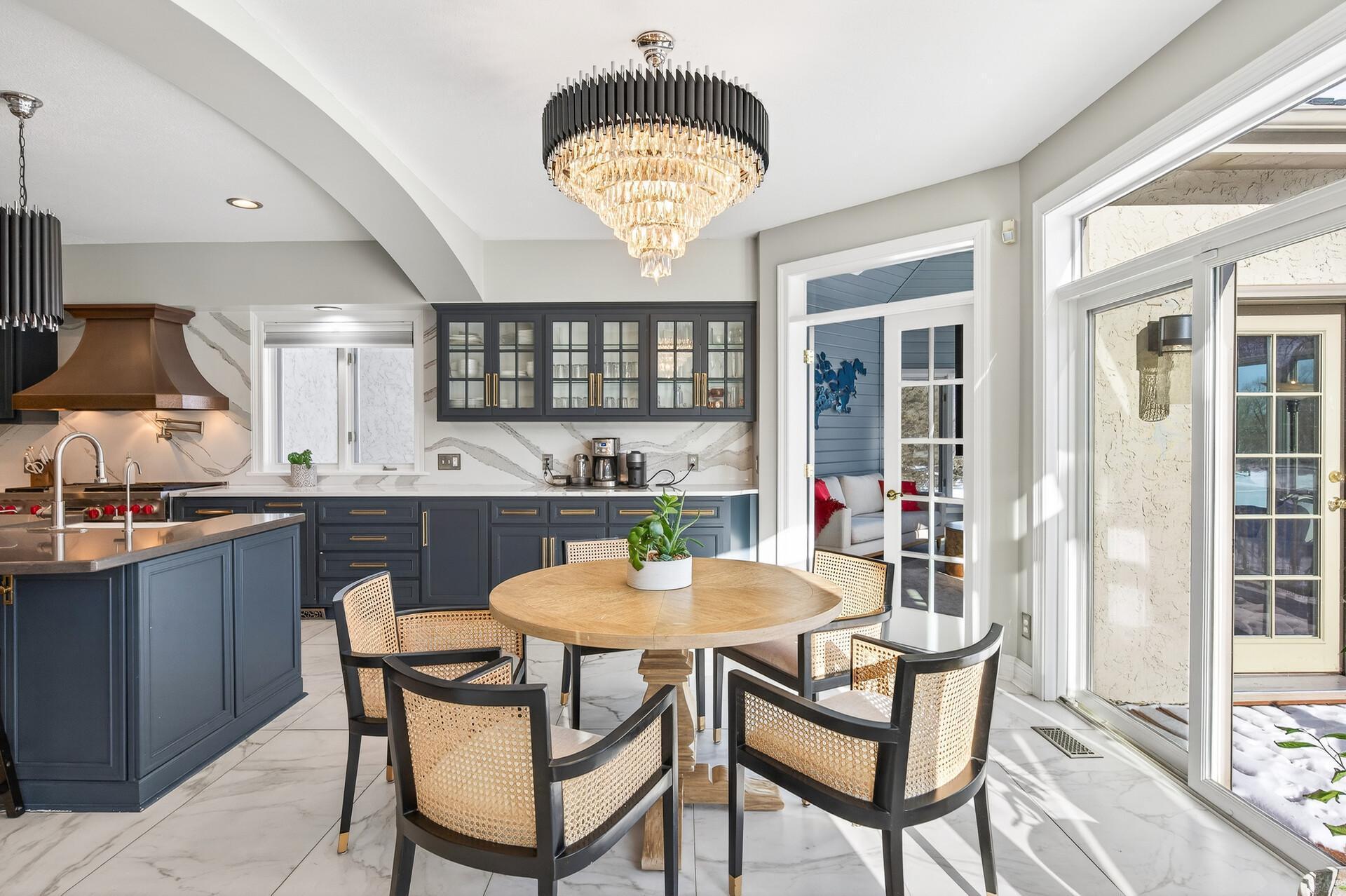 The kitchen flows seamlessly into the informal dining area, accented by a statement chandelier and direct access to the expansive deck—perfect for indoor-outdoor entertaining—as well as the sunroom.