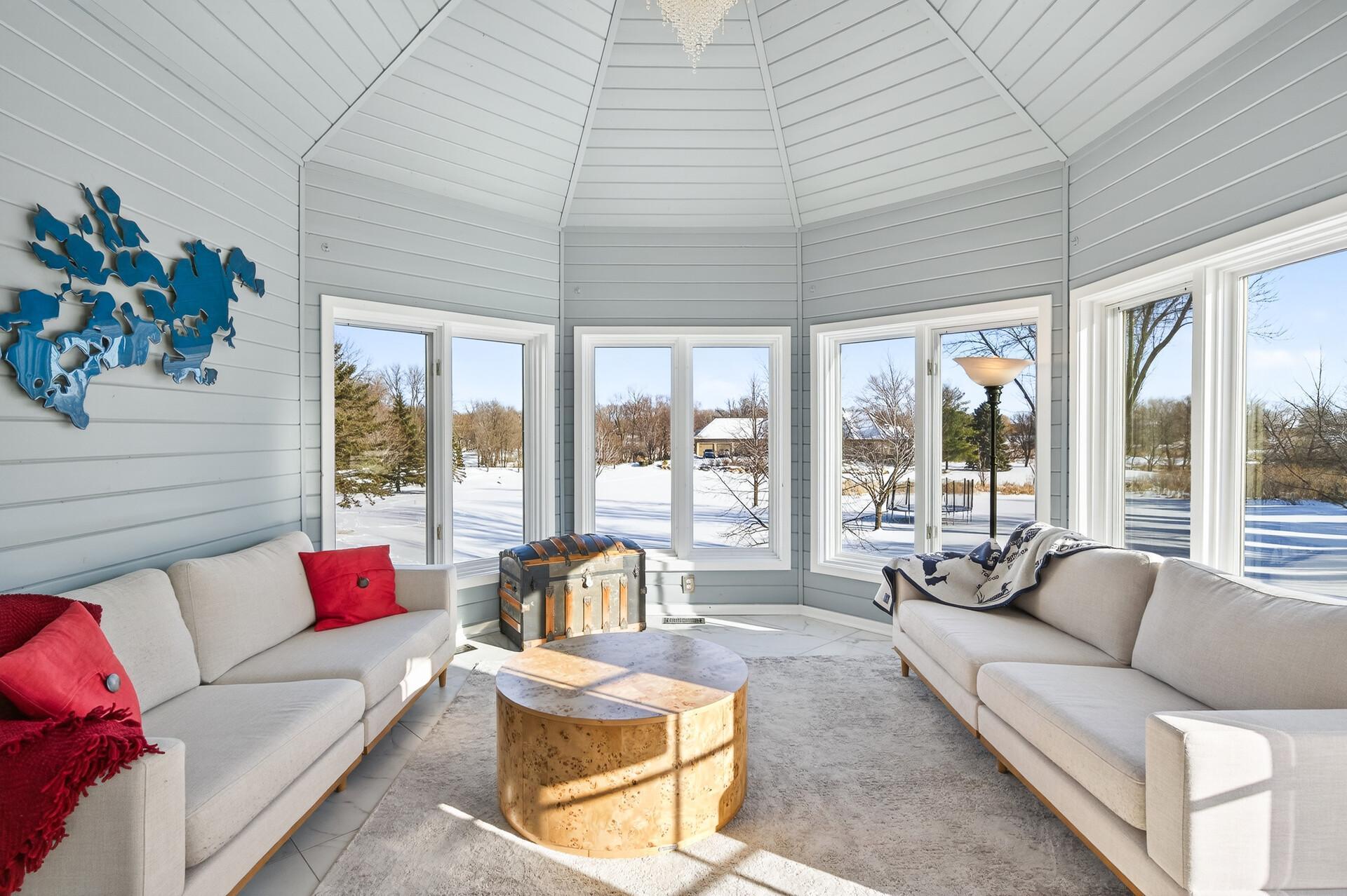 The sunroom is filled with natural light and showcases marble flooring, glass French doors, walls of windows, and a beautiful chandelier, creating an inviting space to relax or entertain.