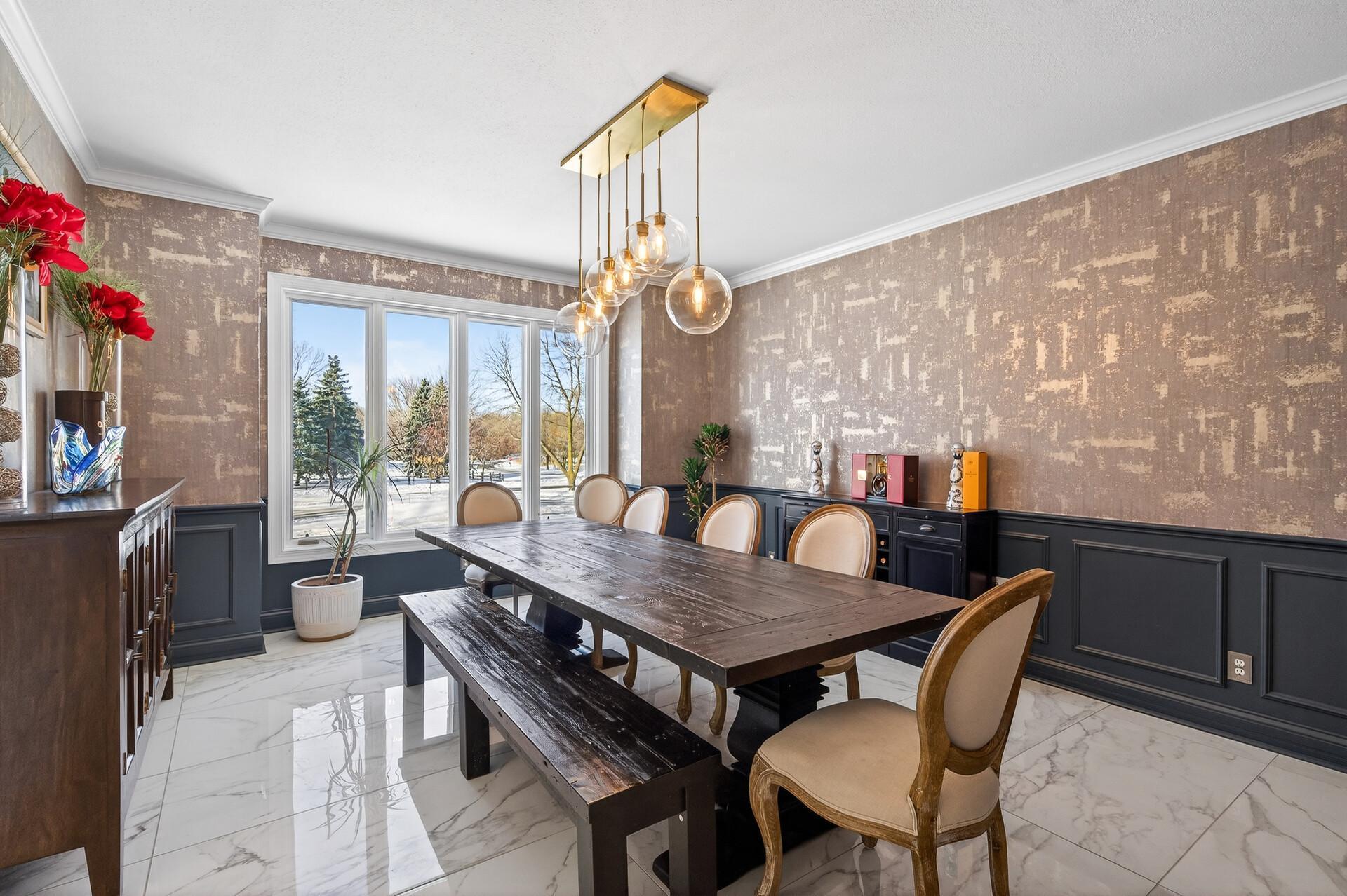 The home’s formal dining room features elegant marble flooring, a large front-facing window that fills the space with natural light, and a beautiful statement light fixture.