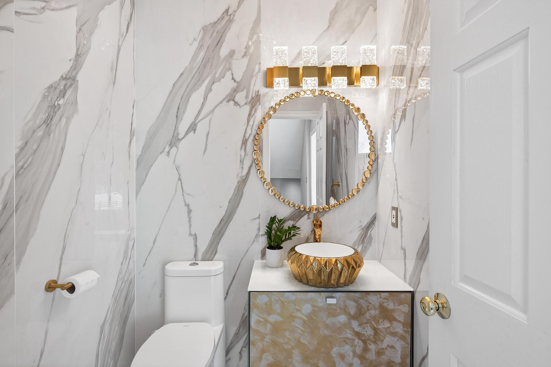 French doors connect the space back to the foyer, and a conveniently located half bathroom nearby is finished with marble floors and walls, a single vanity, and elegant gold-accented fixtures.