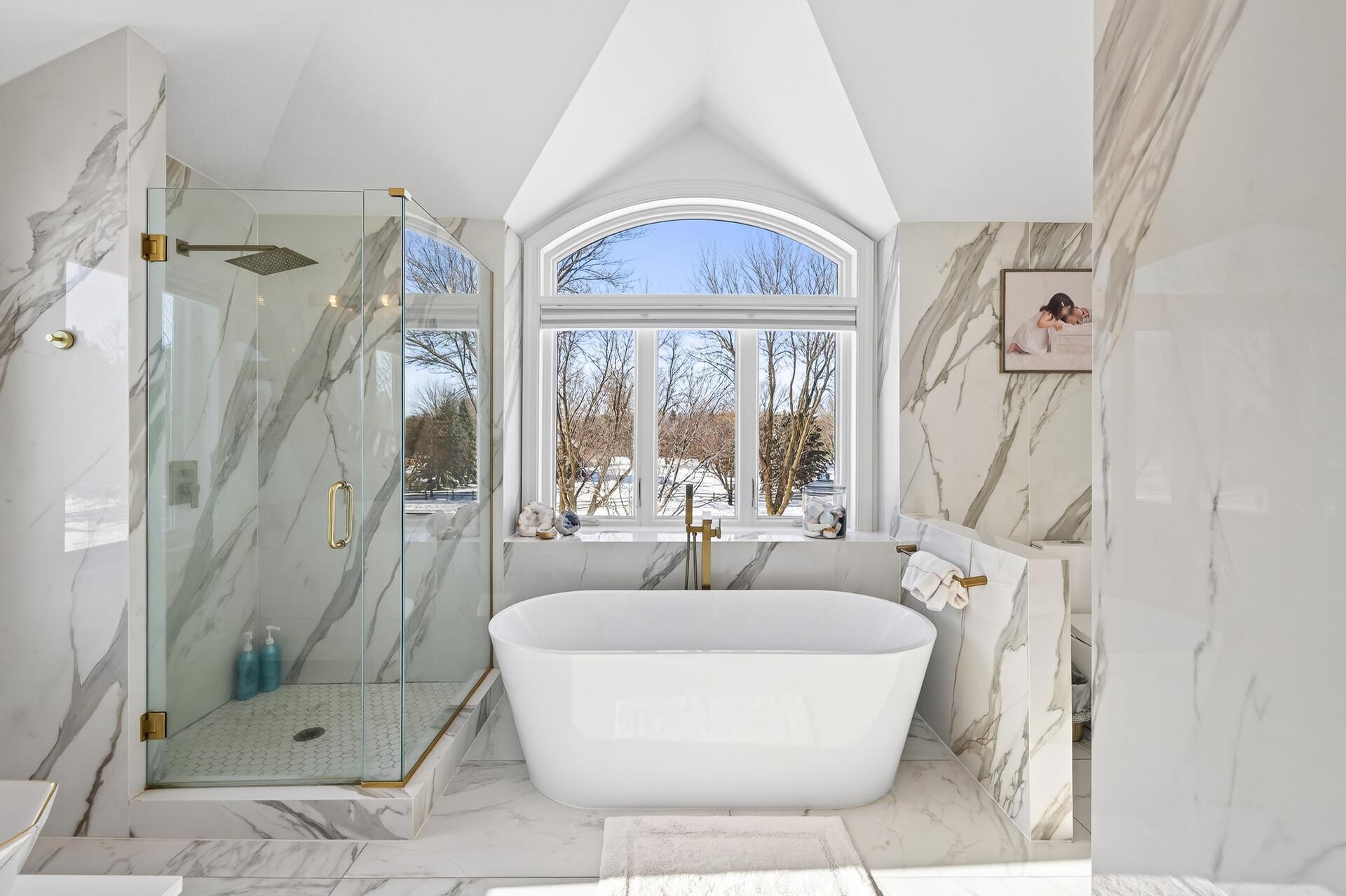 The private primary bathroom feels spa-like, complete with a soaking tub, walk-in shower, marble floors and walls, and a double vanity.