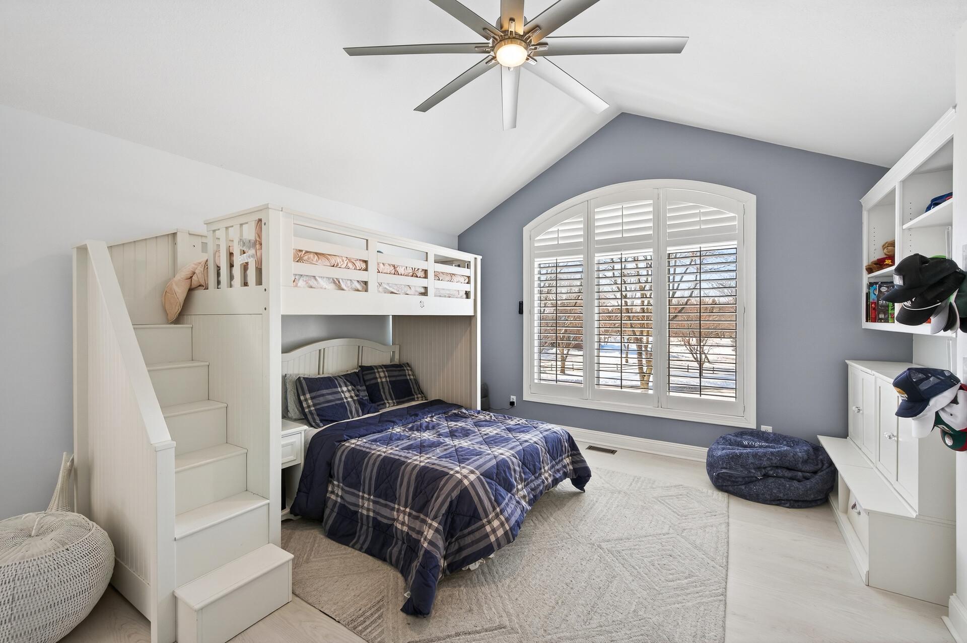 Bedroom two features a vaulted ceiling, modern ceiling fan, luxury plank flooring, large window, built-in shelving, and a spacious with built-ins.