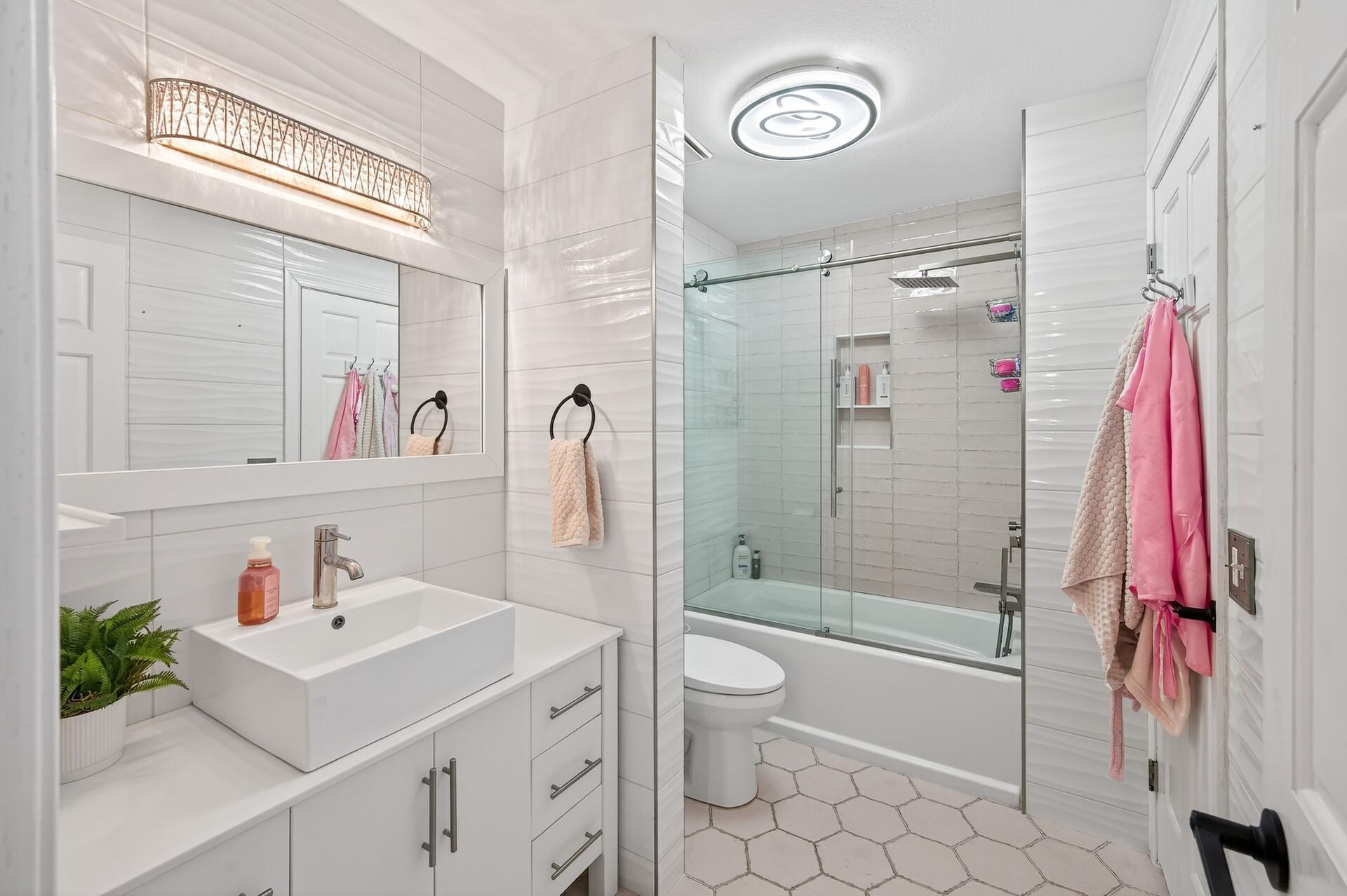 Just steps away is a convenient walk-through full bathroom featuring pink tile floors, tile surround, a tub/shower combination, and a single vanity.