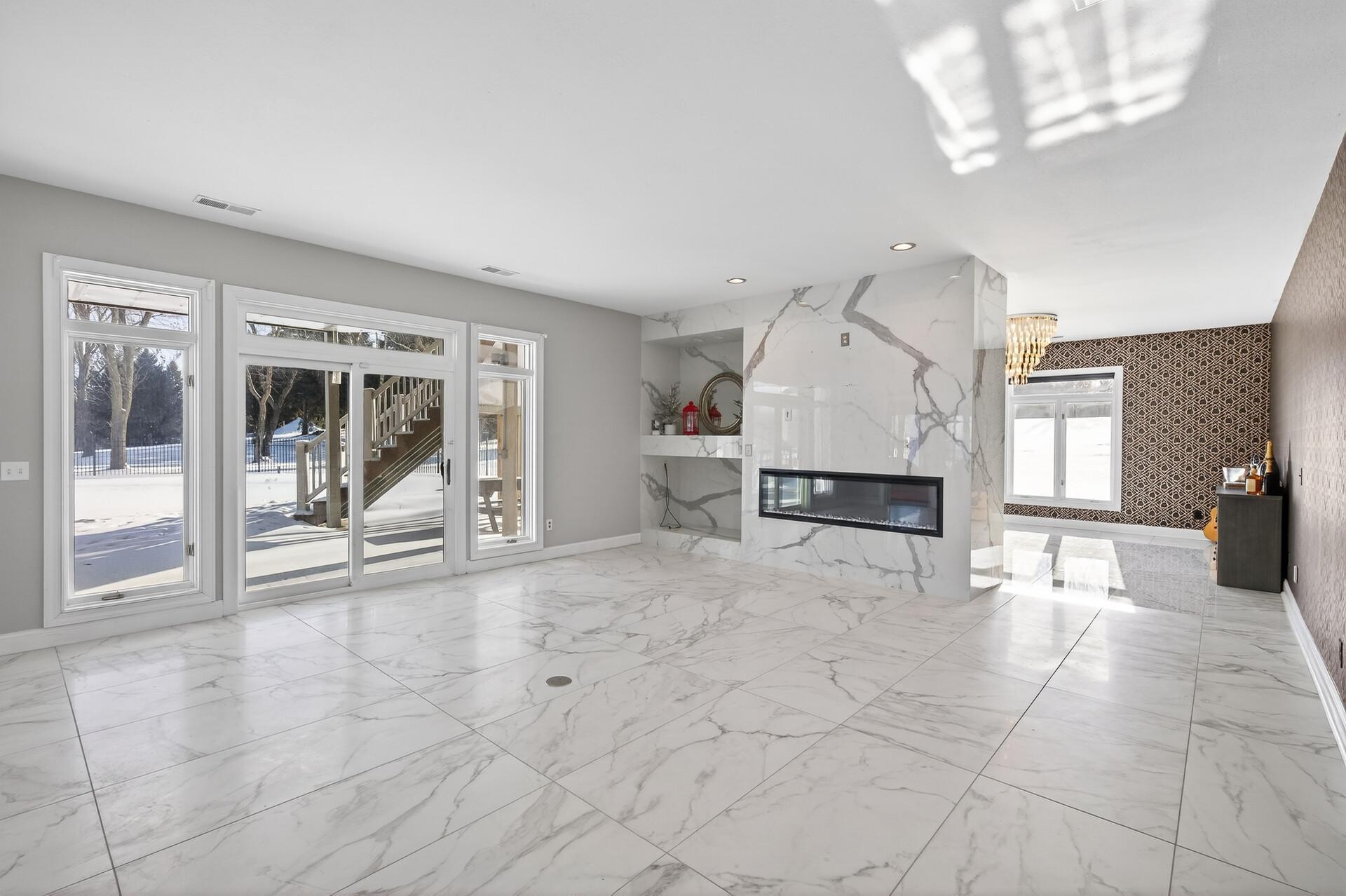 The lower level is truly an entertainer’s dream, featuring a spacious family room with marble flooring, an electric wall fireplace framed by a striking marble surround with custom shelving, and walkout access to the expansive patio and pool.