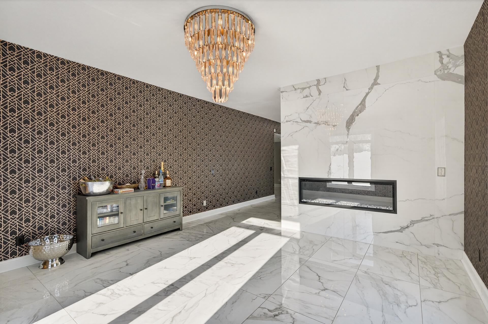 The sitting area shares the double-sided fireplace and offers marble floors, a statement chandelier, and large windows that flood the space with natural light.