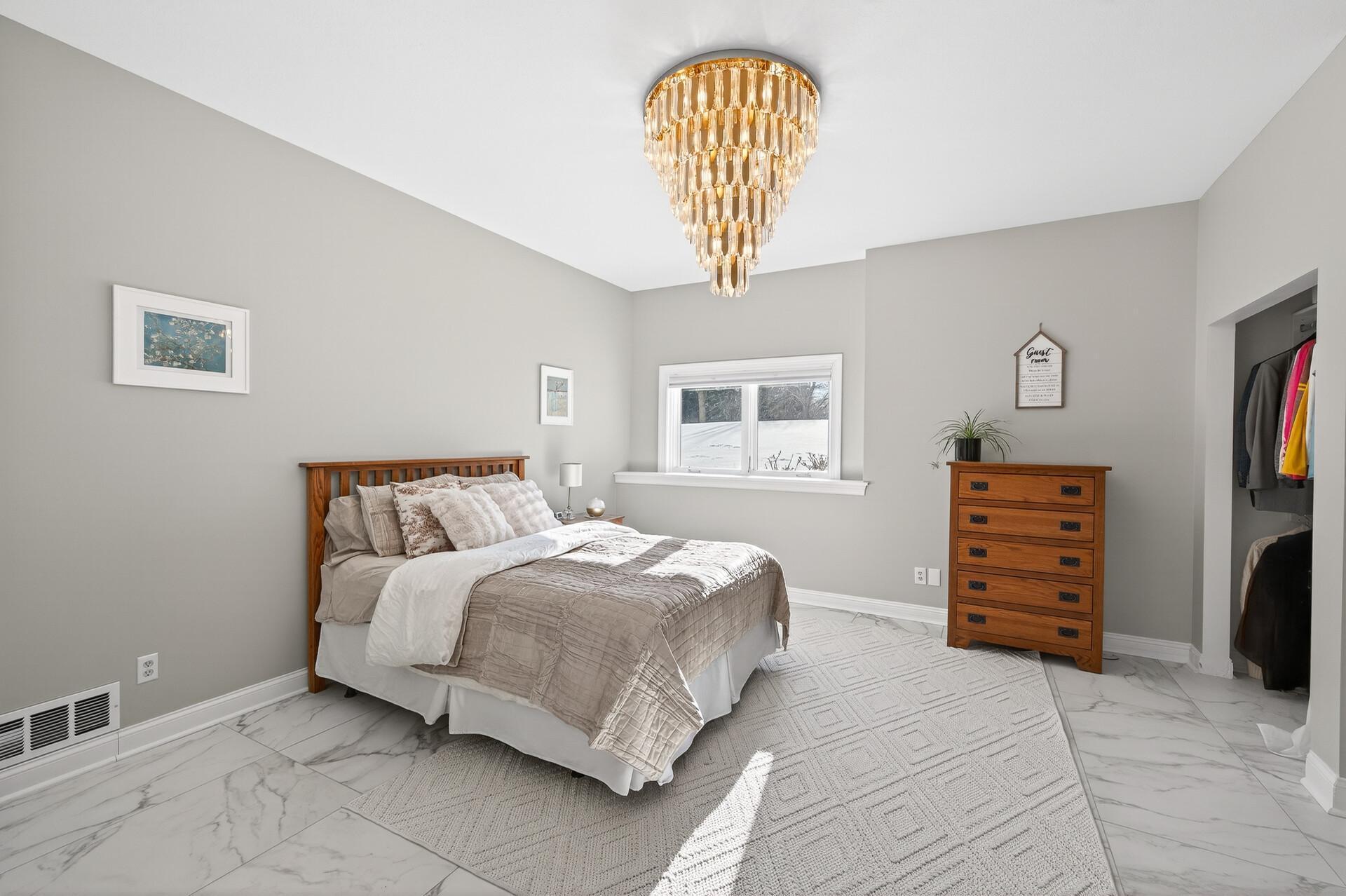 Bedroom five, located on the lower level, showcases a standout chandelier, marble flooring, double closets, and lookout windows.