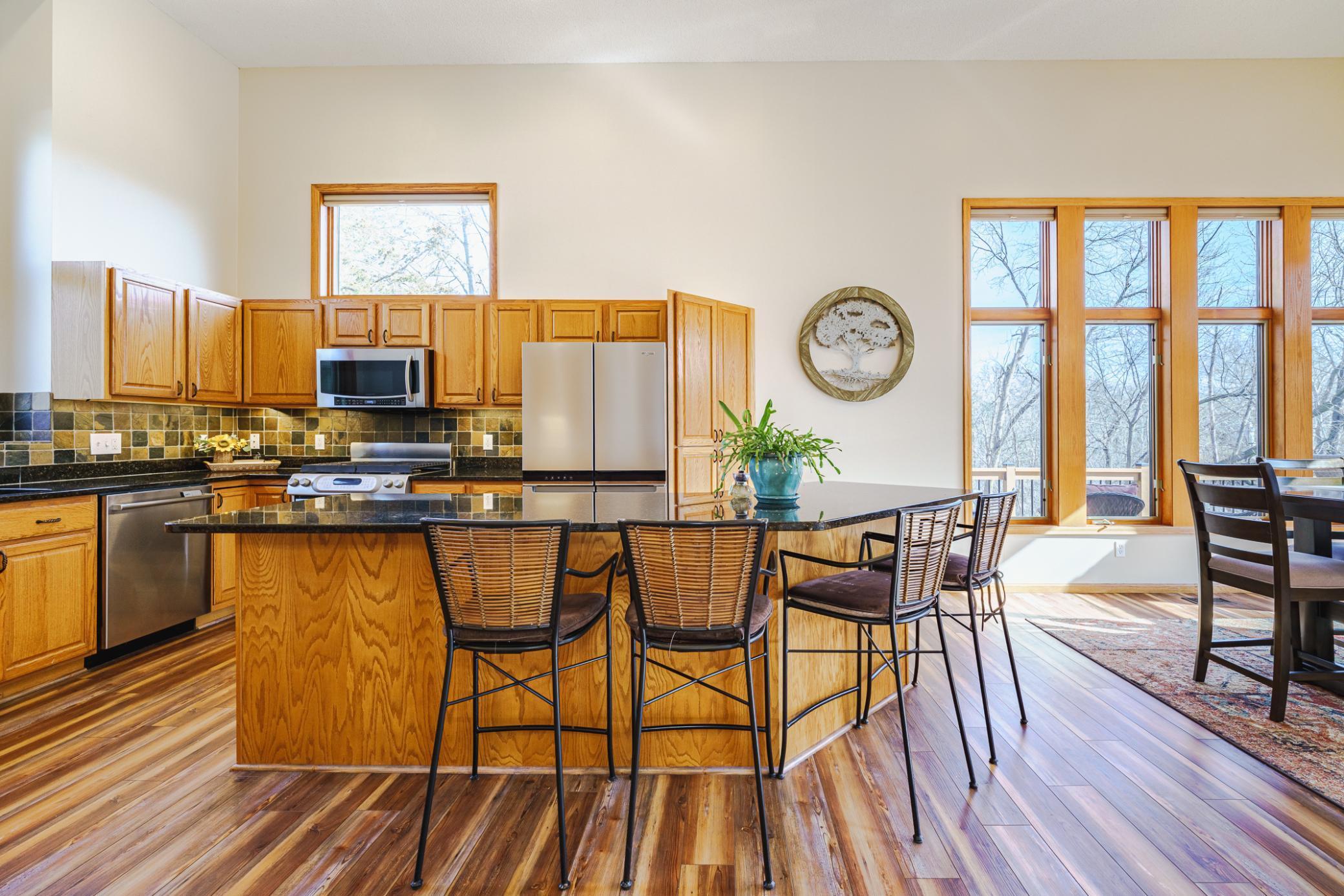 An angled granite island provides abundant countertop space, and there is a tile backsplash. There is also an organization desk. The kitchen opens to the dining room with walls of windows and a door to the wraparound deck.