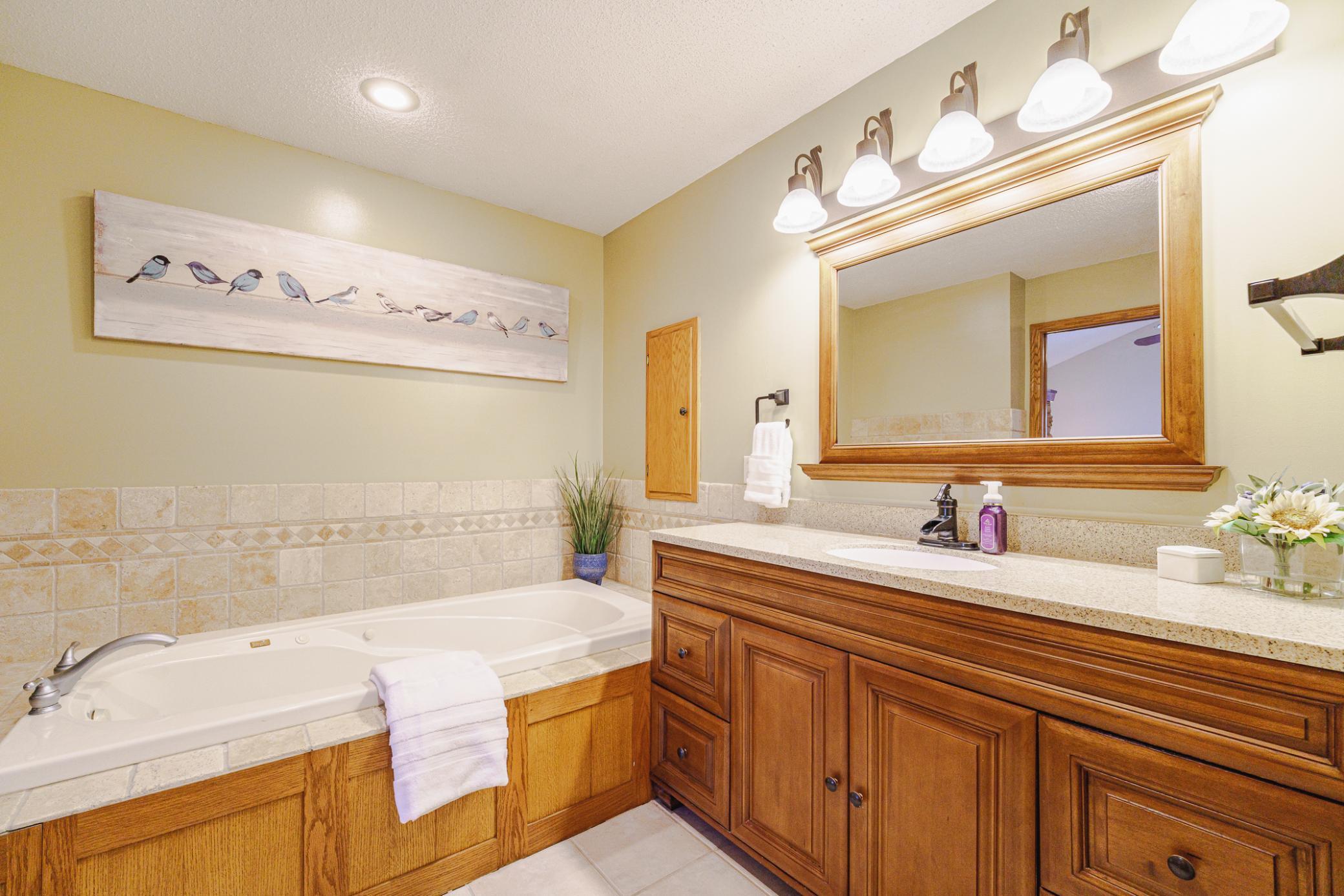 The bathroom has a jetted tub, an elevated-height vanity with a granite counter, and tile flooring.