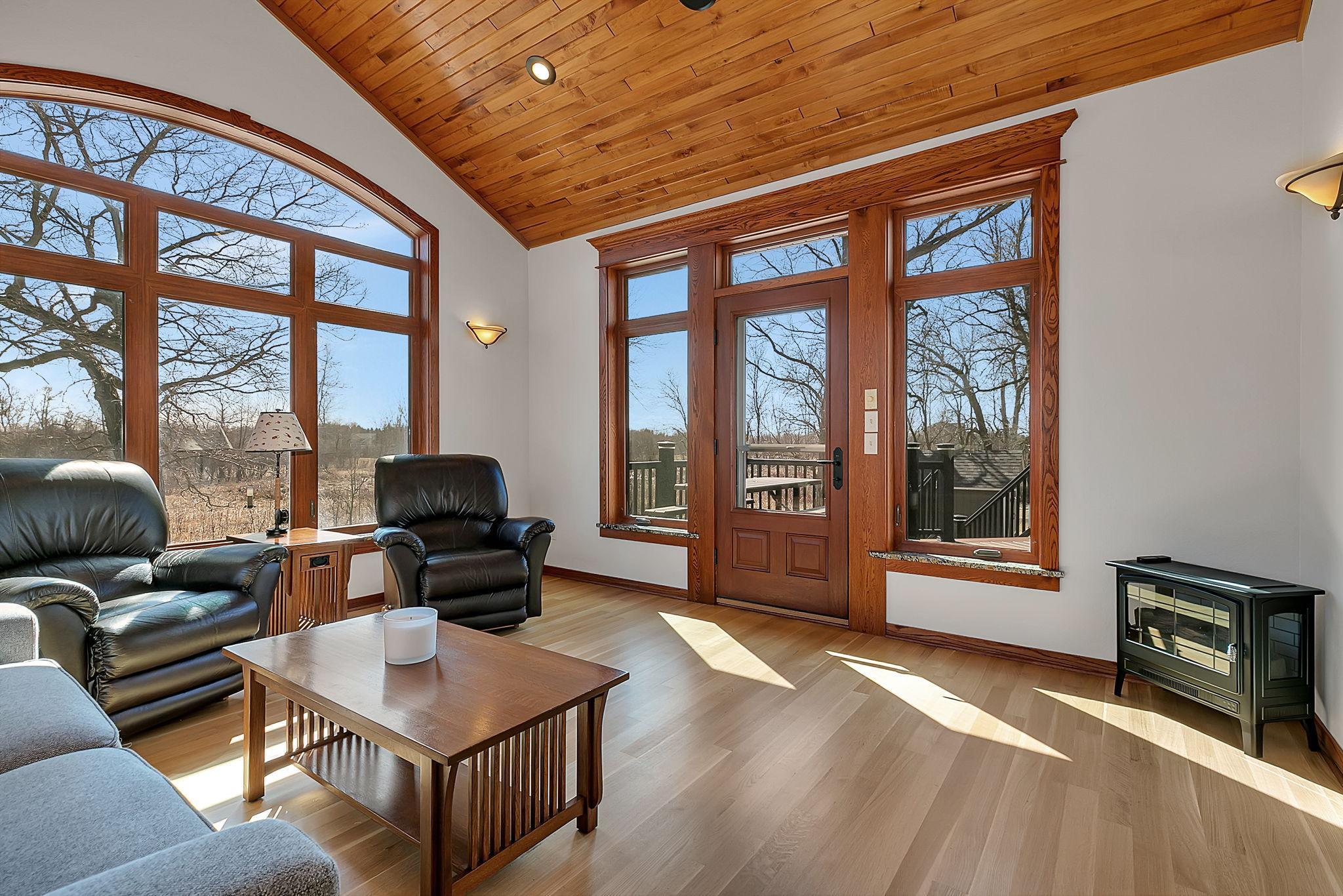 A warm and inviting sunroom with a vaulted wood ceiling, expansive windows, and rich natural light, offering peaceful outdoor views and a cozy place to relax year-round.