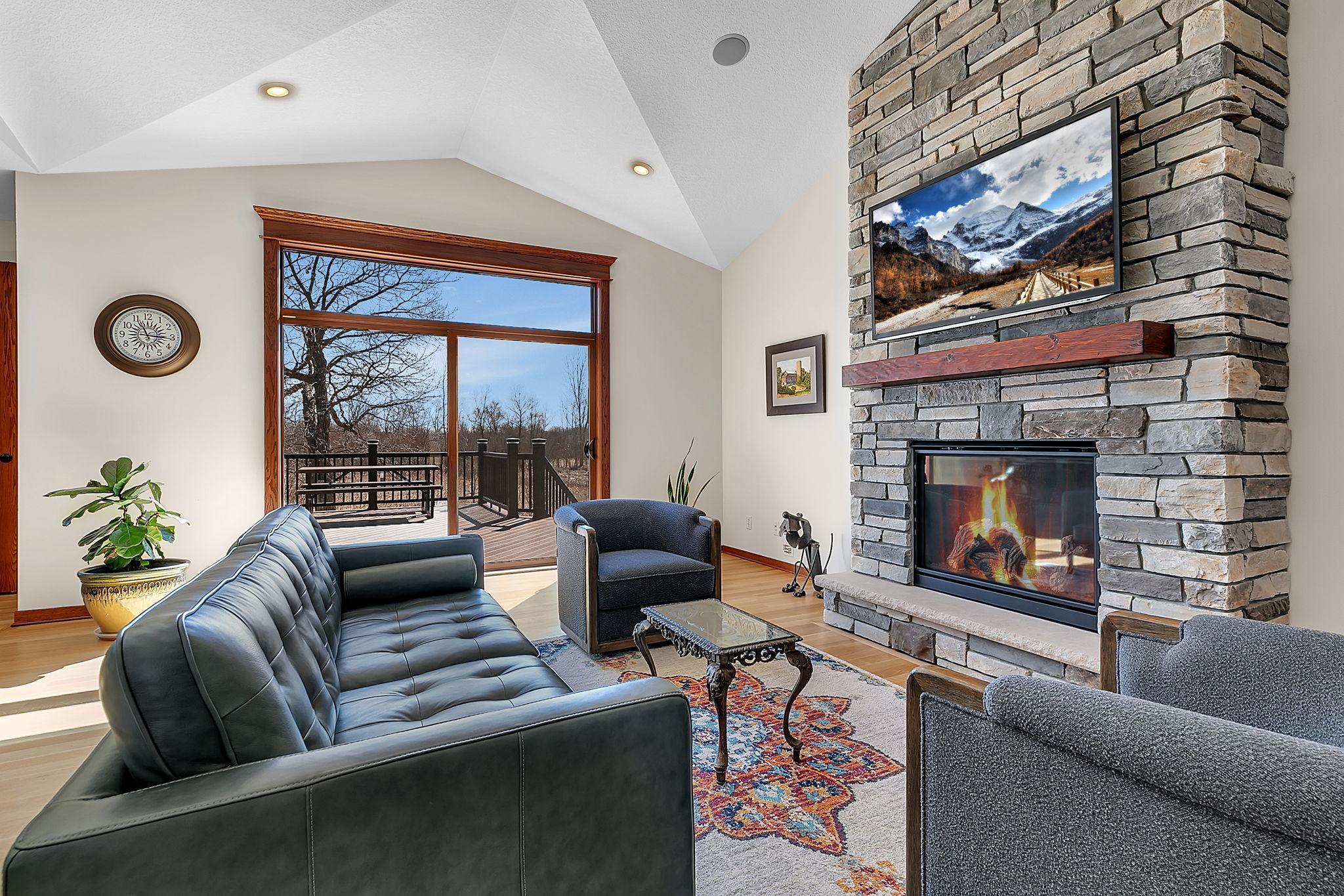 A welcoming living room with a stone-surround fireplace and mantel, flowing effortlessly through expansive patio doors to the deck for indoor-outdoor living.