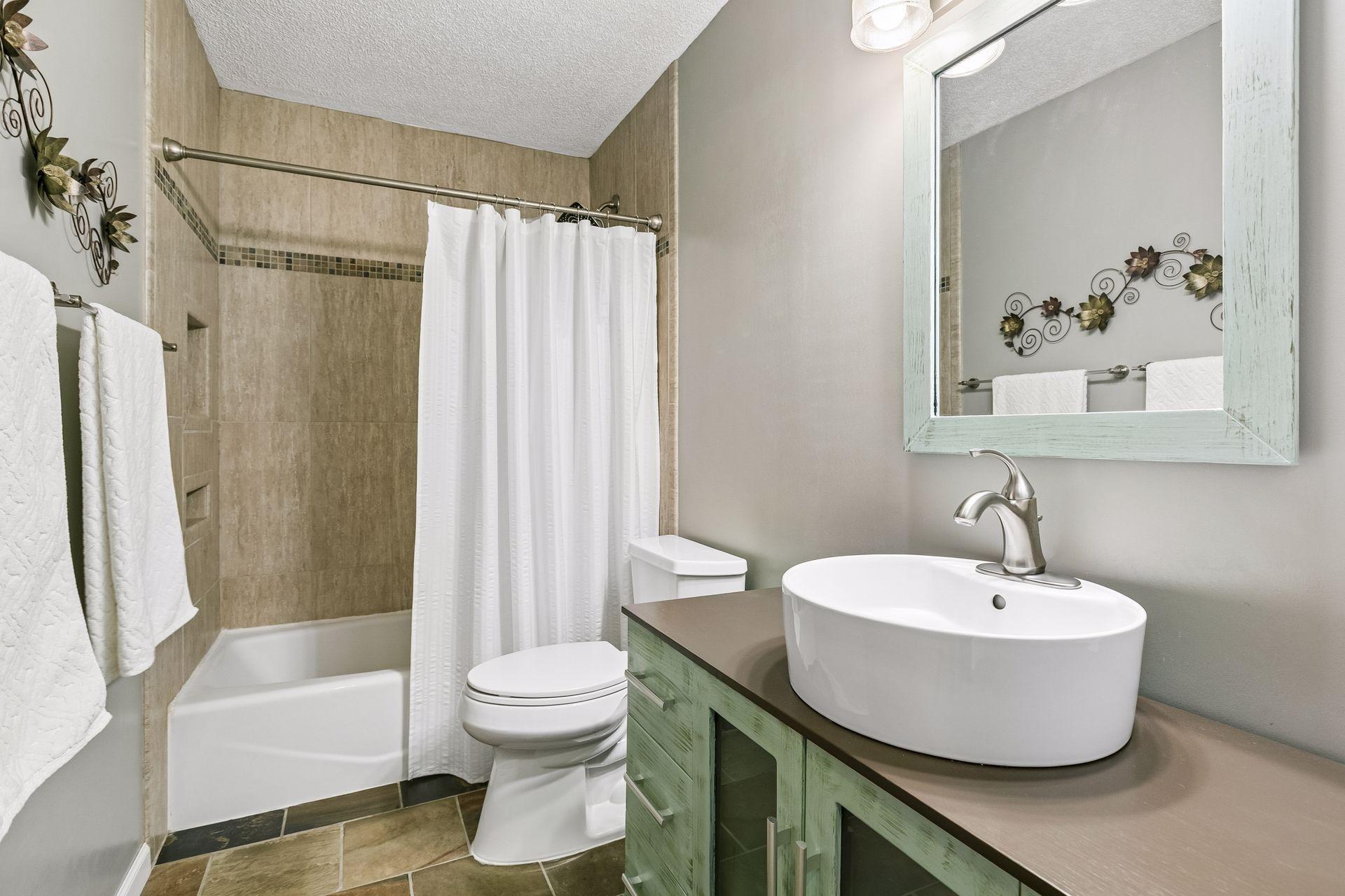 Well-appointed full bath with ceramic tile floors and tub surround, complemented by an updated vanity and modern bowl sink.