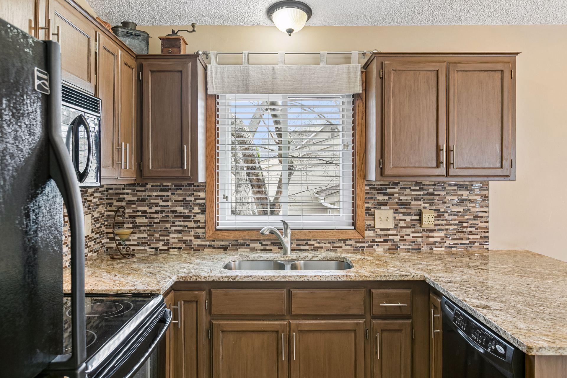The chef's workspace is outlined with granite countertops and tile backsplash, stainless sink & kitchen window.