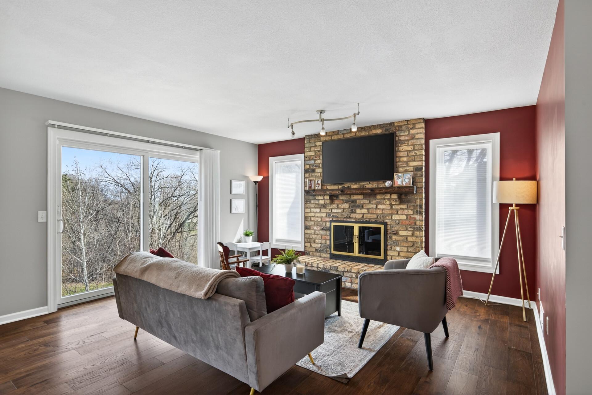 Main-level living room with large windows, brick surround wood burning fireplace, and sliding door for future deck.