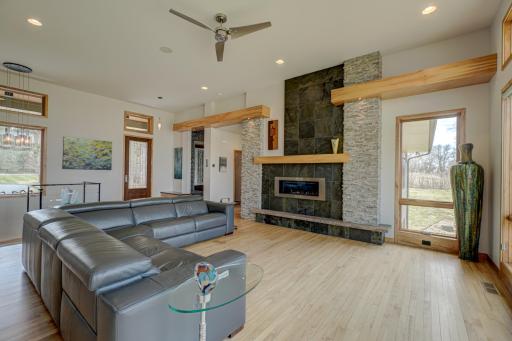 Expansive windows frame the surrounding landscape, while a striking fireplace with stone detail and wood accents anchors the living room.