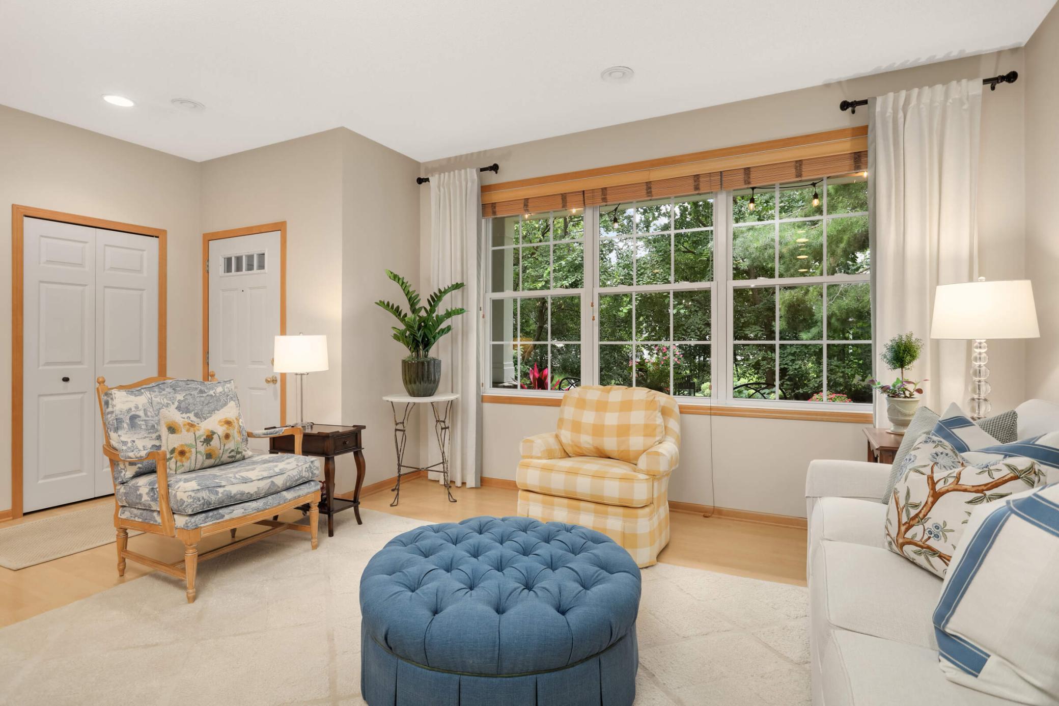 The living room flows to the covered porch, showcasing a stunning yard framed by mature trees and colorful flower beds.