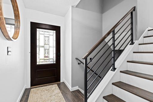 Step inside and the craftsmanship speaks immediately. A beautifully crafted glass entry door, rich dark stair treads, and custom architectural railings that make every arrival feel like a moment.