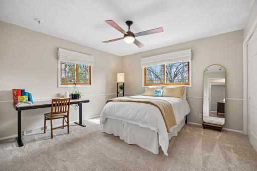 A spacious corner bedroom with windows on two walls, offering great natural light along with built-in storage and a separate closet