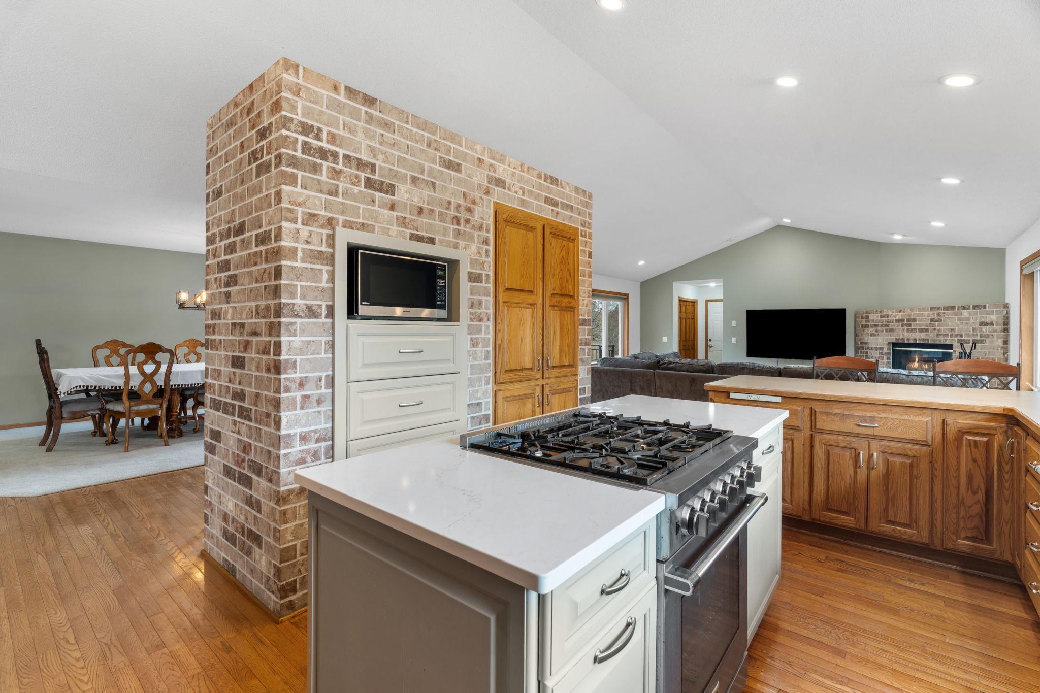 Open concept kitchen features a floor to ceiling brick column, all flowing seamlessly into the dining and living areas with hardwood floors throughout