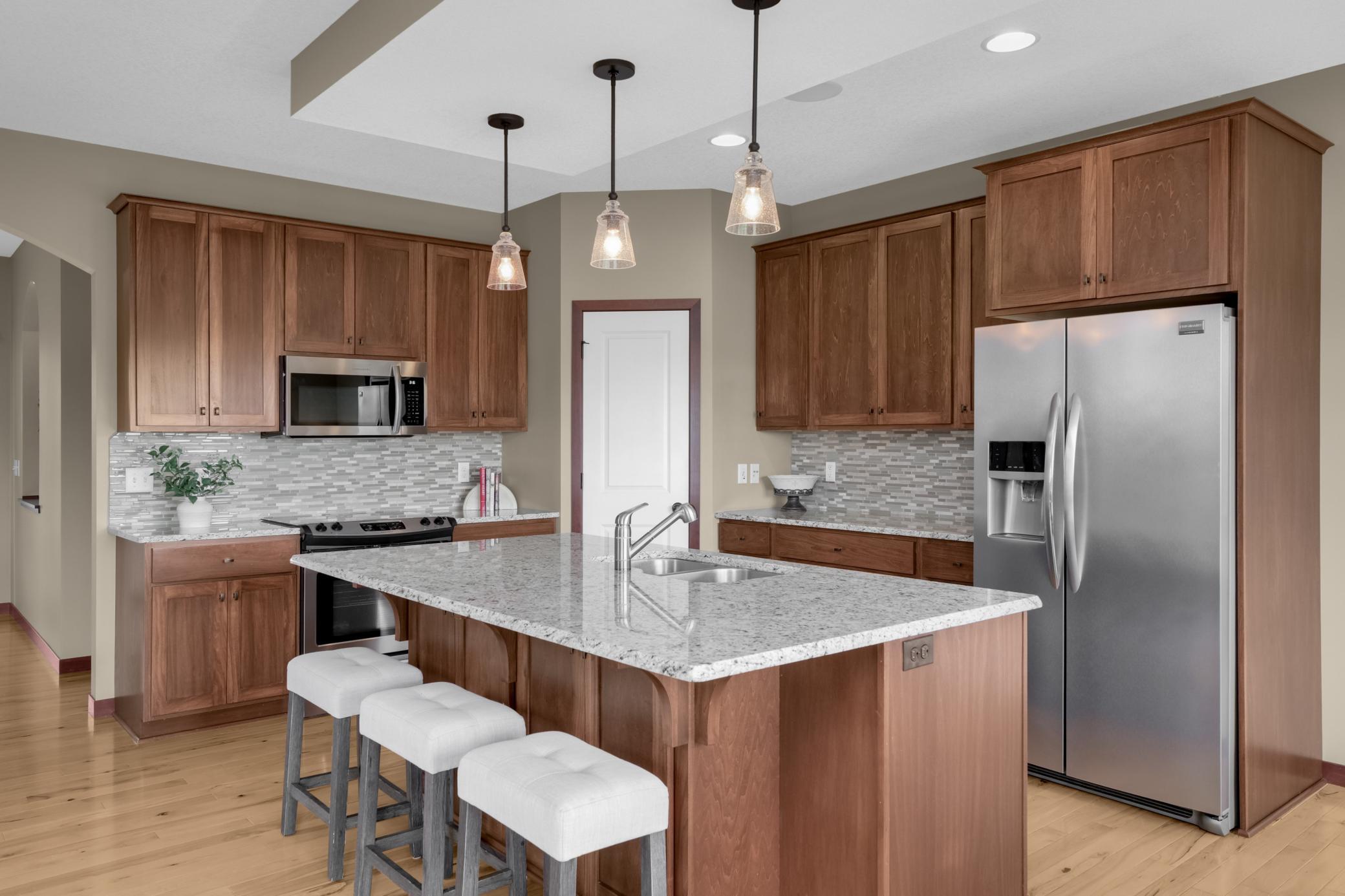 Stylish kitchen showcasing granite countertops, stone backsplash, stainless steel appliances, and a walk-in pantry for added storage.