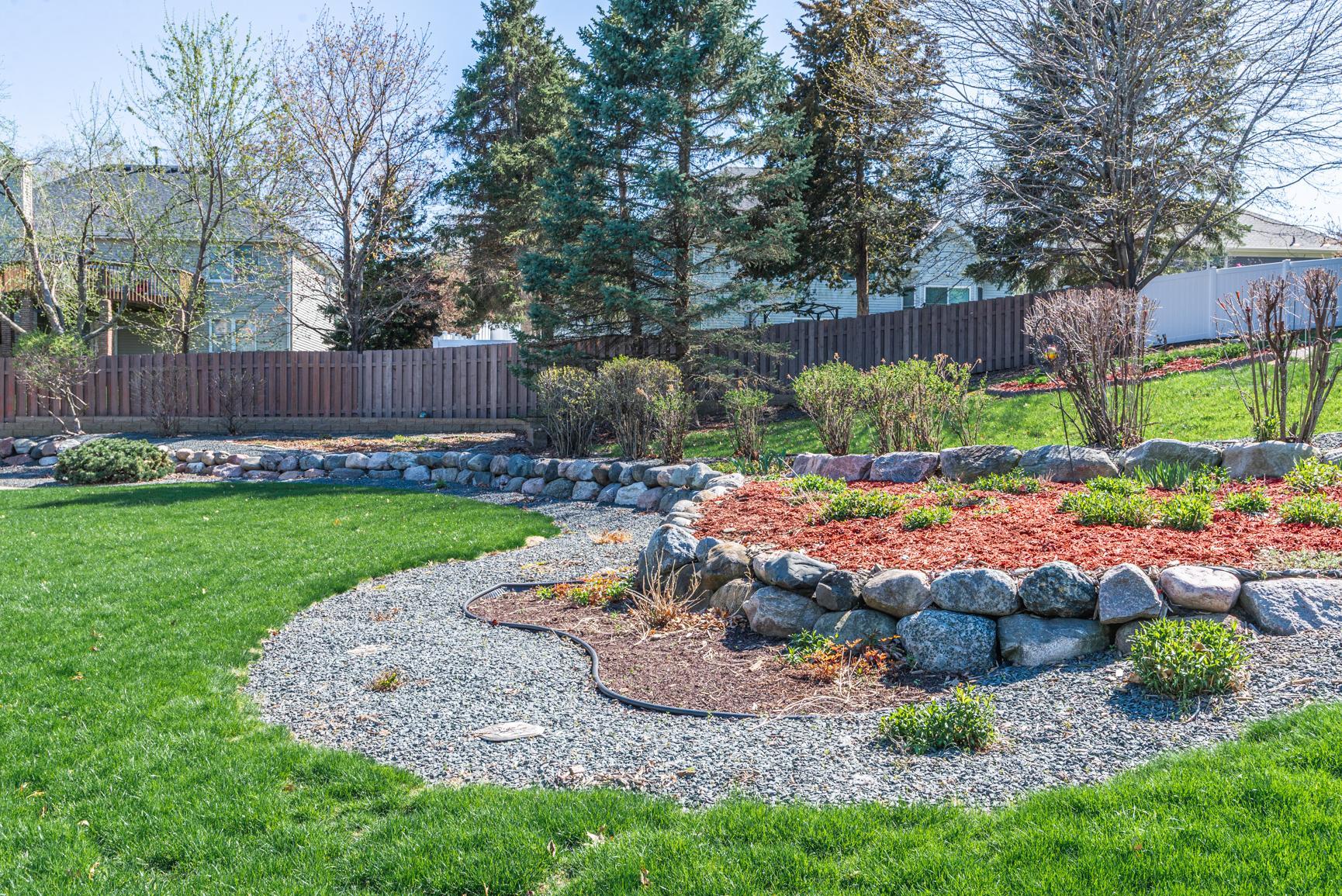 This large backyard with a tiered rock wall sweeps across the back of the lot, creating a picturesque scenery with many perennials in the separated stone and mulched garden areas.