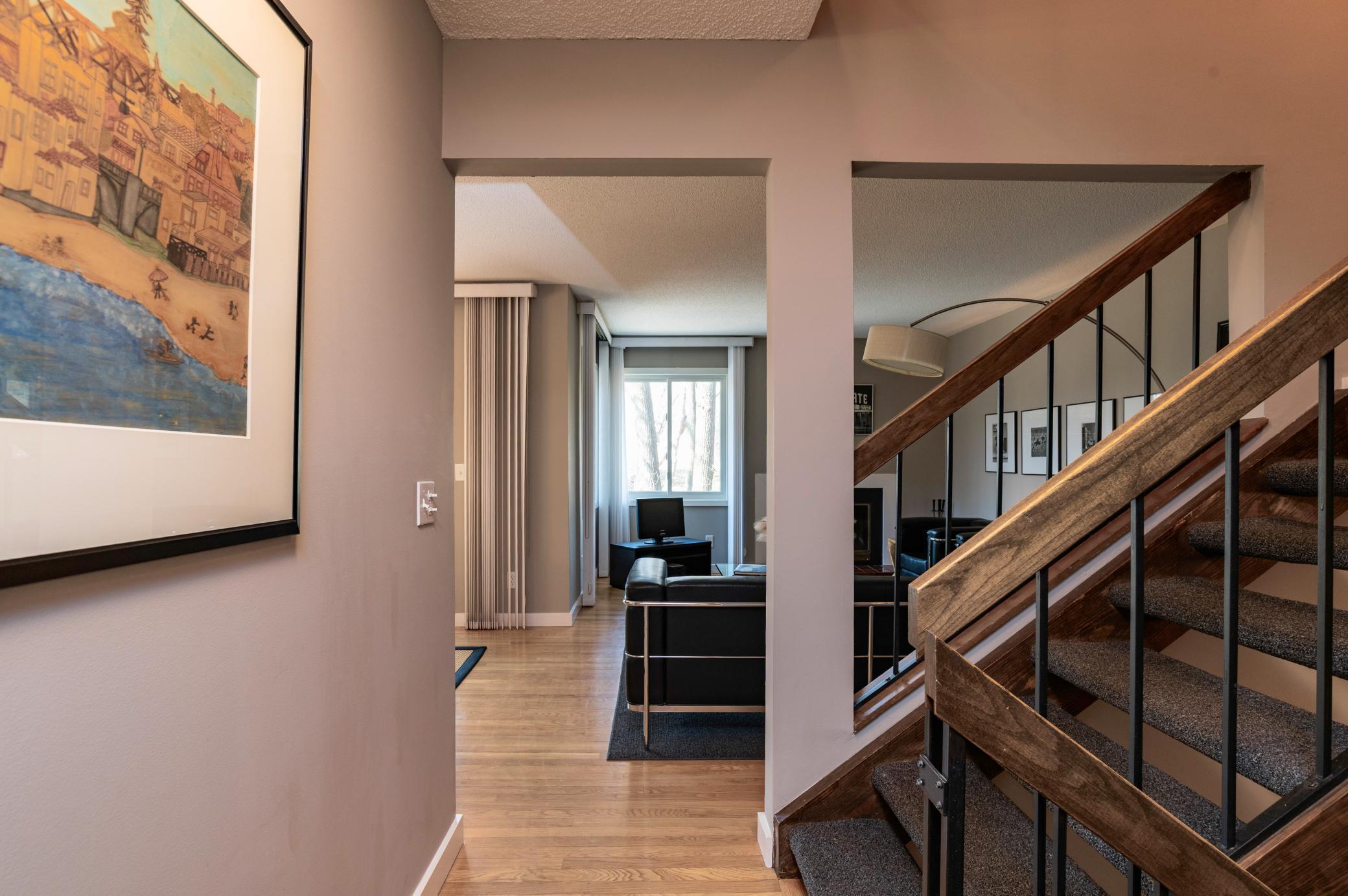 Main level hallway from entry provides access to the kitchen on the left, living room straight ahead and open staircase to both the upper and lower level. Hardwood flooring throughout main level.