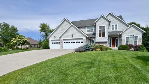 Beautiful curb appeal featuring a lush green lawn and mature landscaping in full bloom. Highlights include a beautiful Japanese Tree Lilac and vibrant perennials, creating a picturesque and welcoming entrance to this elegant home