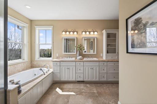 This private bath boasts beautiful stone-topped vanities, designer lighting, and timeless tile accents
