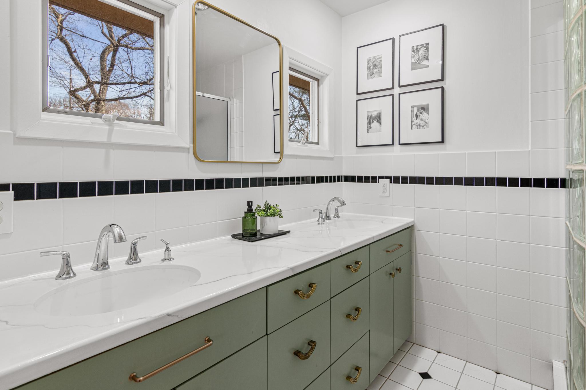 The primary bathroom strikes the perfect balance, thoughtfully updated with a sage green double vanity, brass hardware, and crisp white countertops, while preserving the classic tile detail that gives it character.