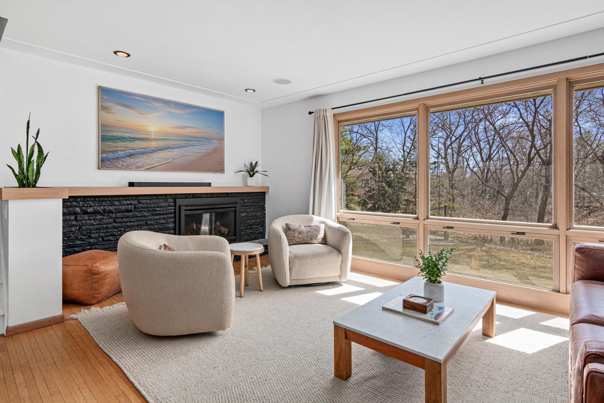 The stacked-stone fireplace grounds the room on one end while the oversized windows dissolve the boundary between inside and out on the other.