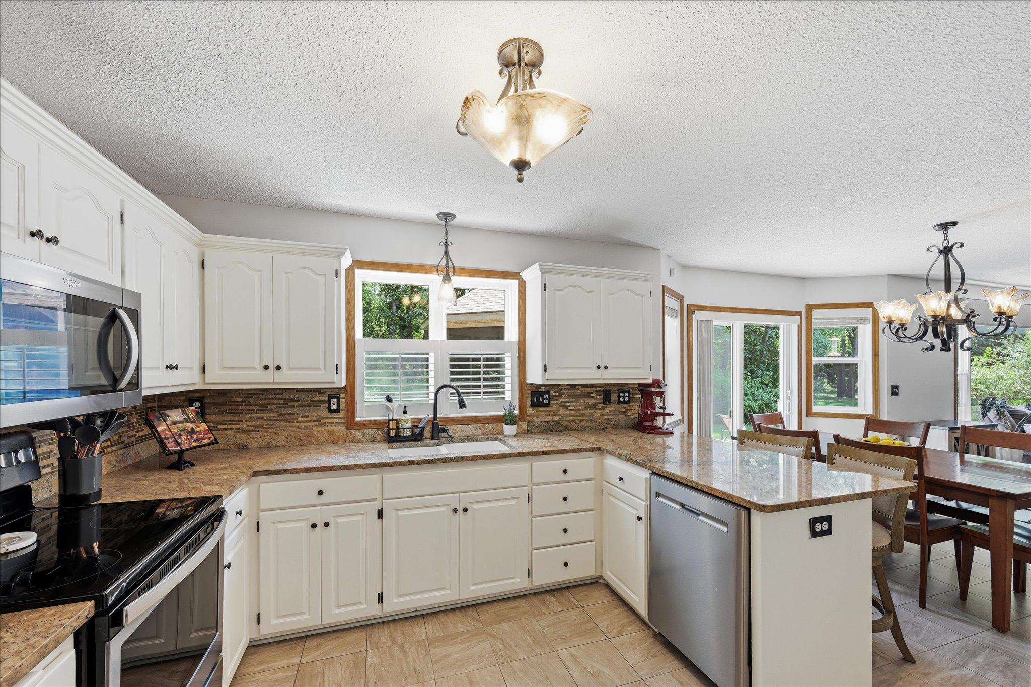 Updated kitchen featuring granite countertops, painted cabinetry, tile backsplash, and built-in wine rack