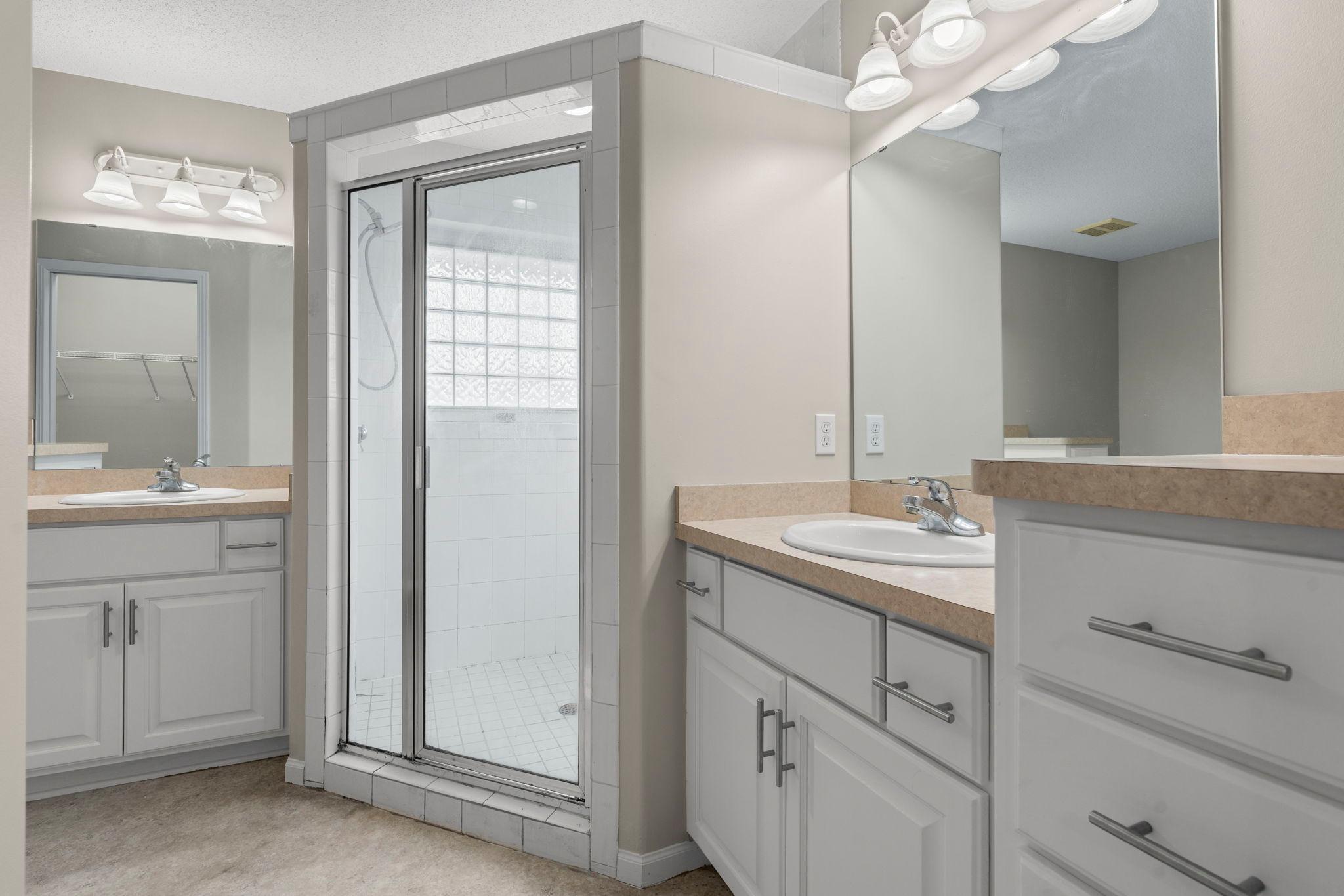 Primary bathroom with large tiled shower and seperate sinks and vanities. Abundance of storage drawers.