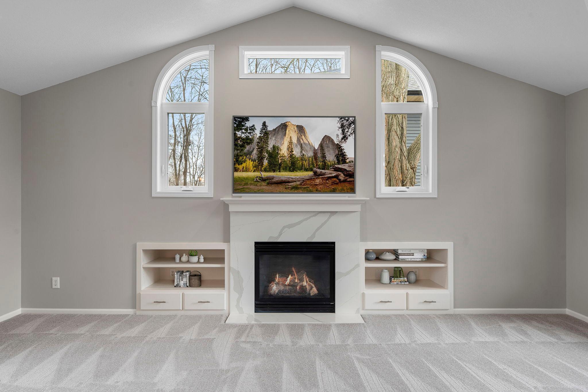 Gorgeous fireplace backdrop with quartz front, accented by unique curved windows! TV / shelves virtually staged to envision the possibility.