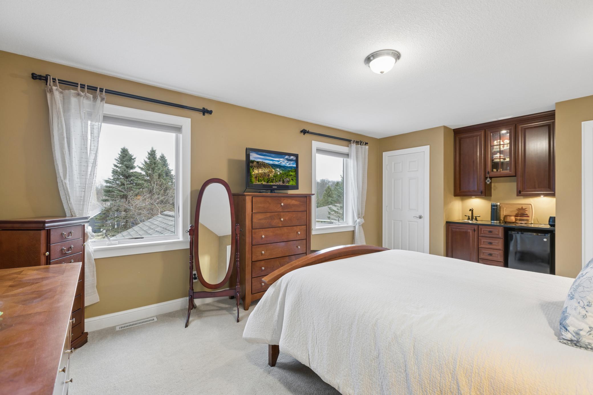 View of the upper level primary bedroom with dual closets a coffee bar and ensuite bathroom.