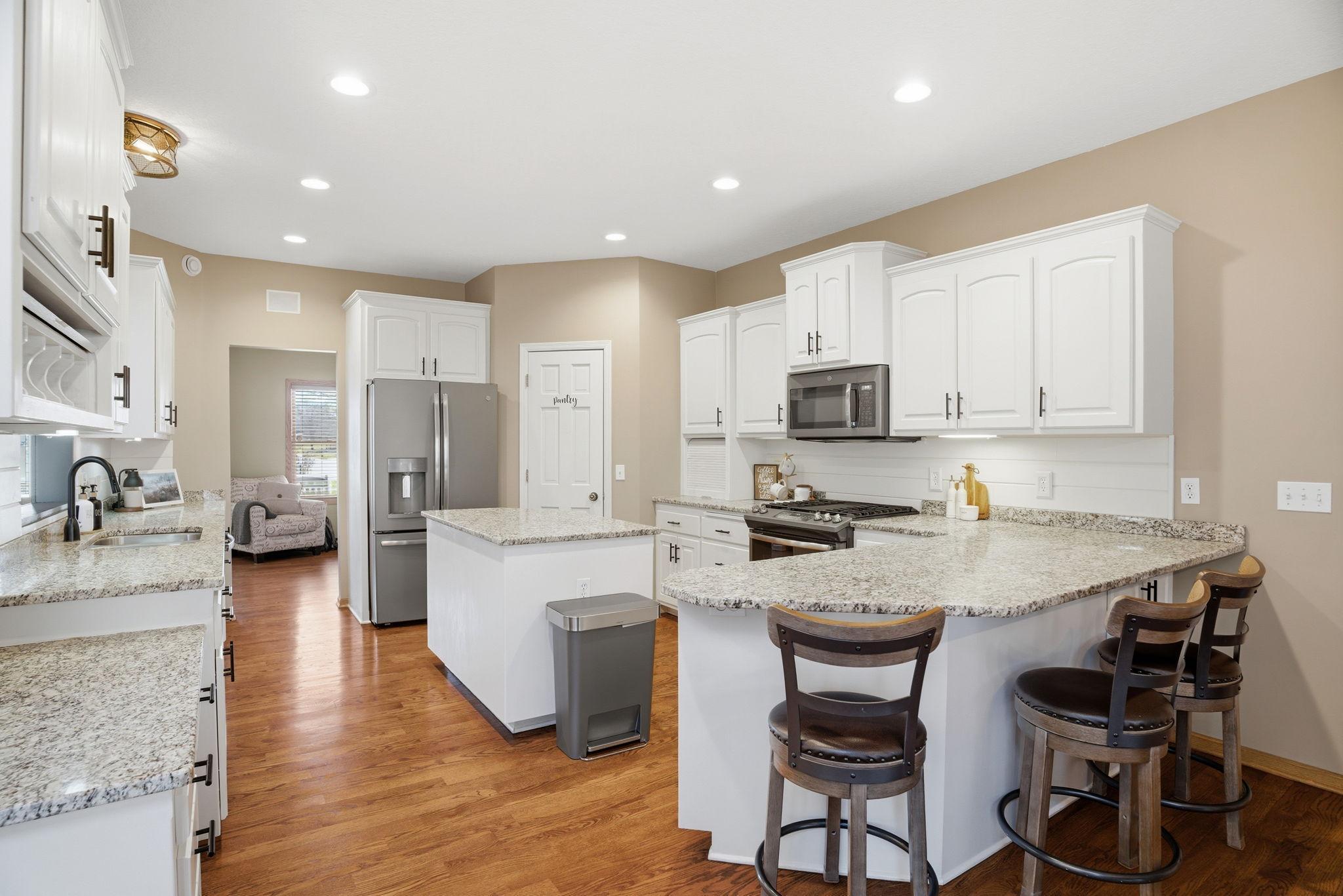 Spacious kitchen boasting a walk-in pantry, elegant granite countertops, recessed lighting, and a center island ideal for meal prep and entertaining. With a peak into the front living room.