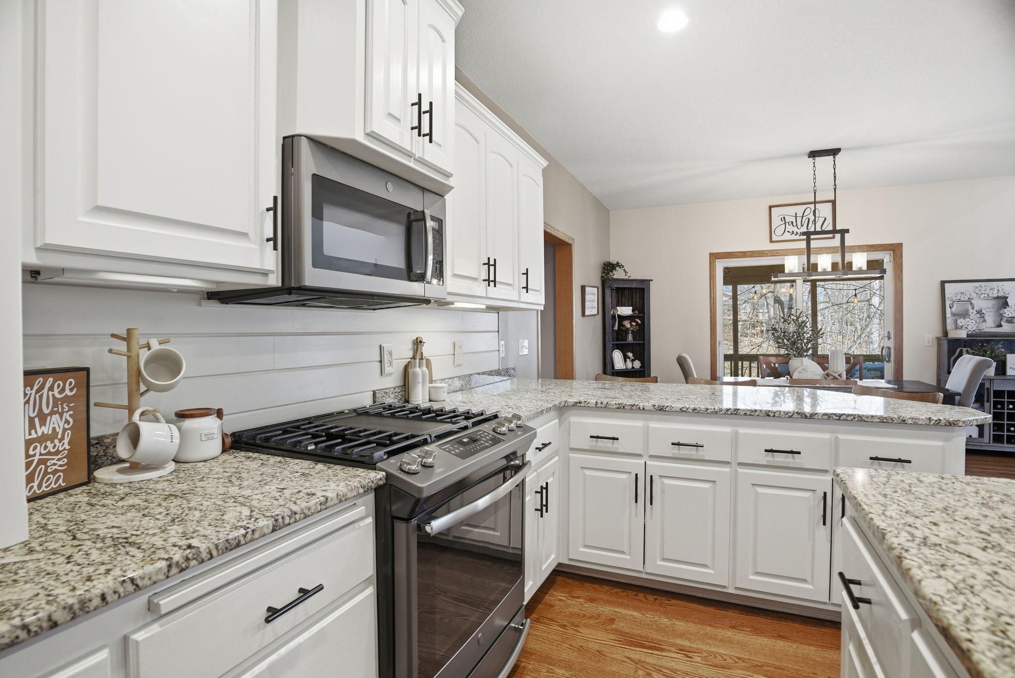 Kitchen features a gas stove, shiplap accents, white cabinets, and granite countertops.