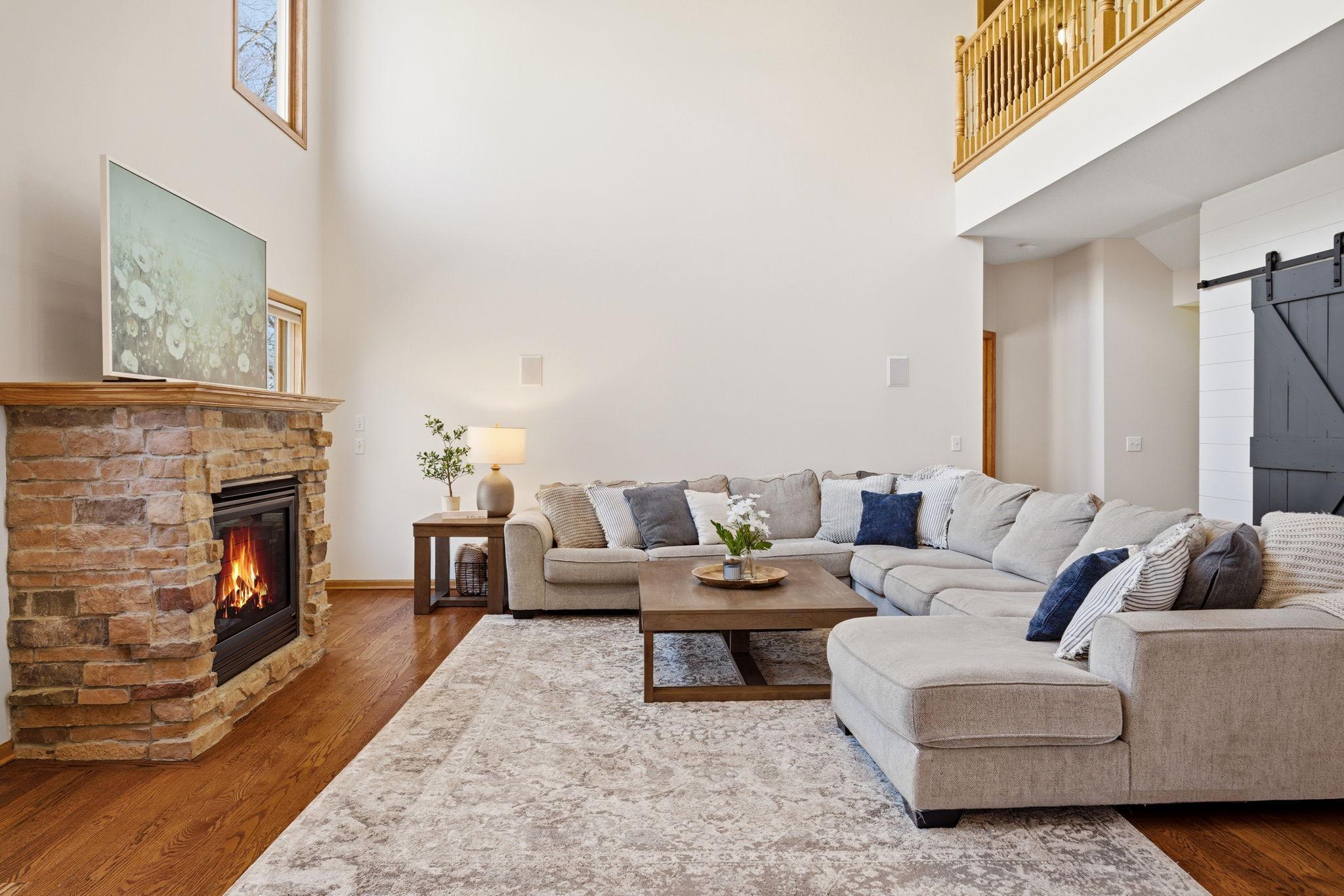 Bright, open two-story great room featuring a cozy gas fireplace, plenty of windows, and peaceful wooded backyard views.