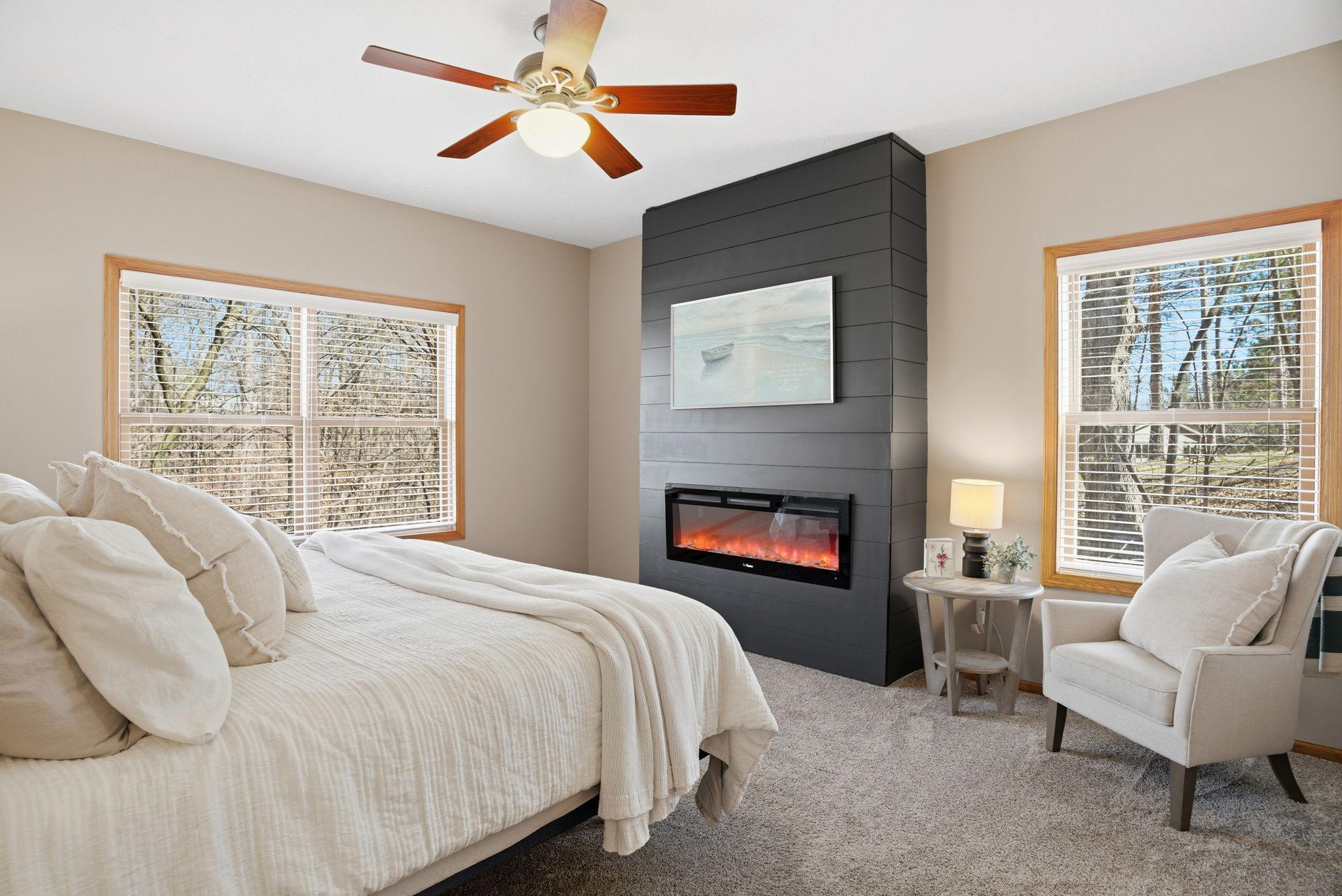 Main-level primary bedroom offers generous space, a charming electric fireplace, and tranquil views overlooking the wooded backyard.