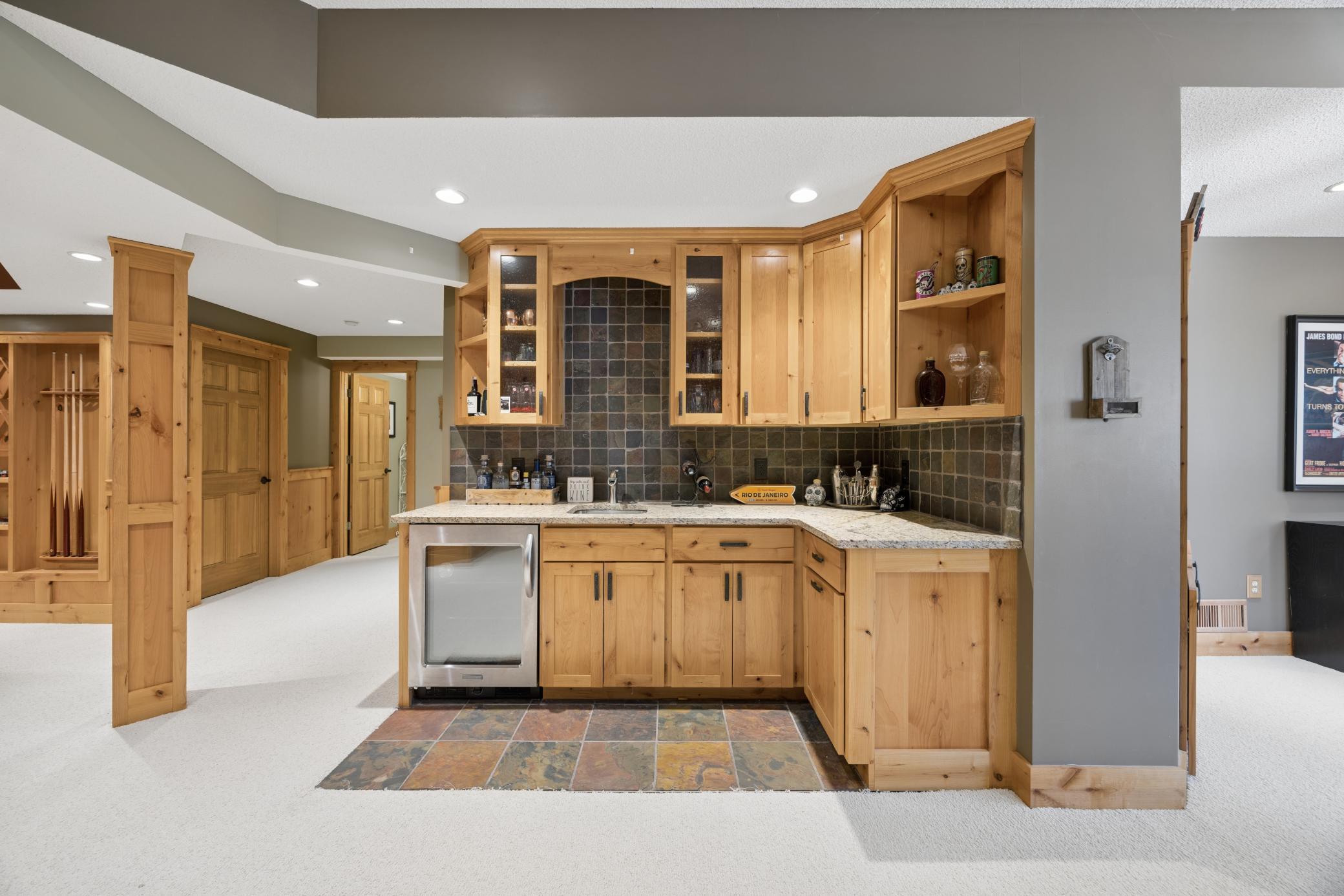 Built-in wet bar with tile floor and backsplash, granite countertop, and stainless steel mini fridge.