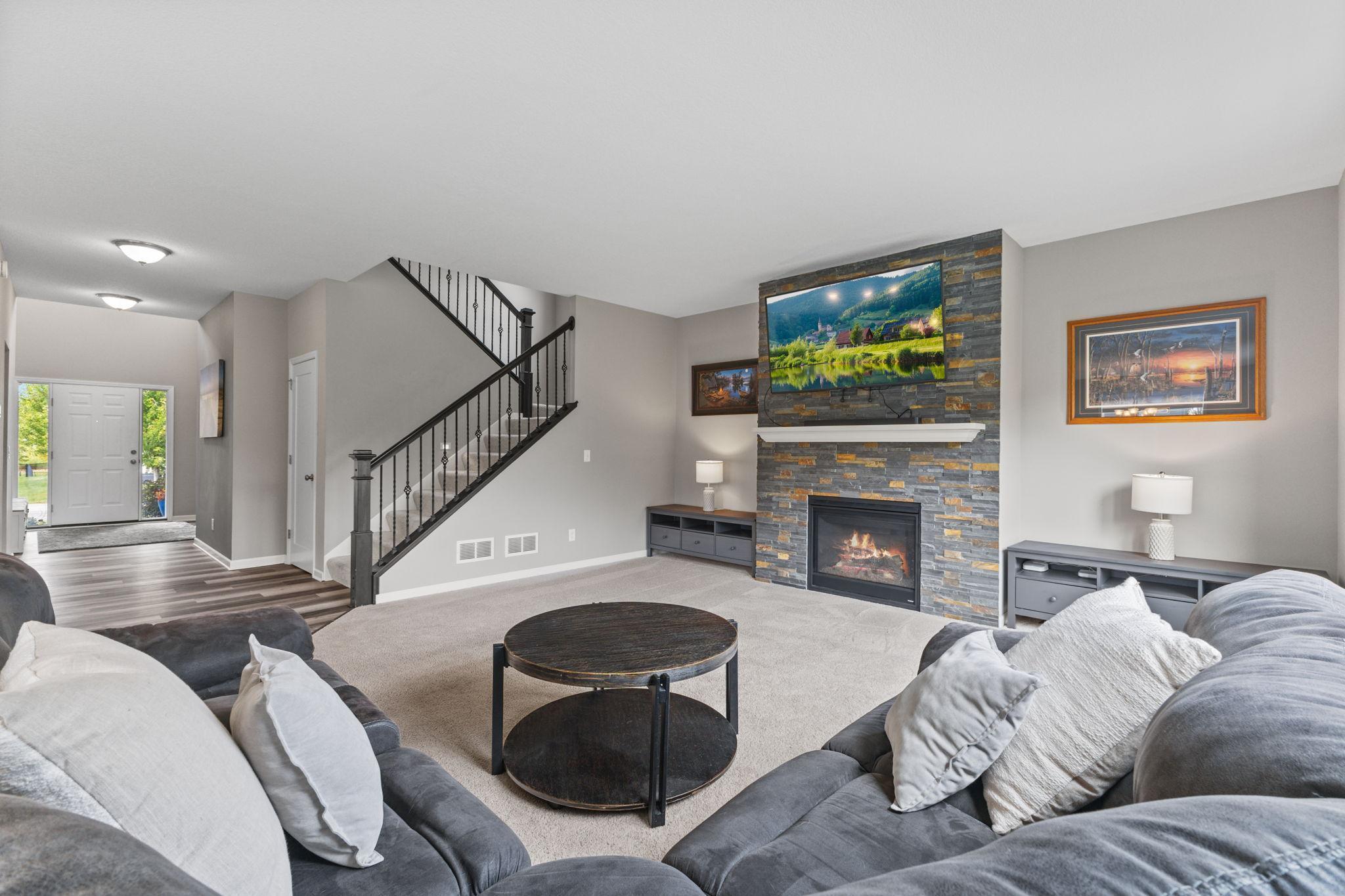 The staircase leads from the main living room to an upper-level landing overlooking the foyer, with a spacious primary suite, three additional bedrooms, a full bath, and laundry.