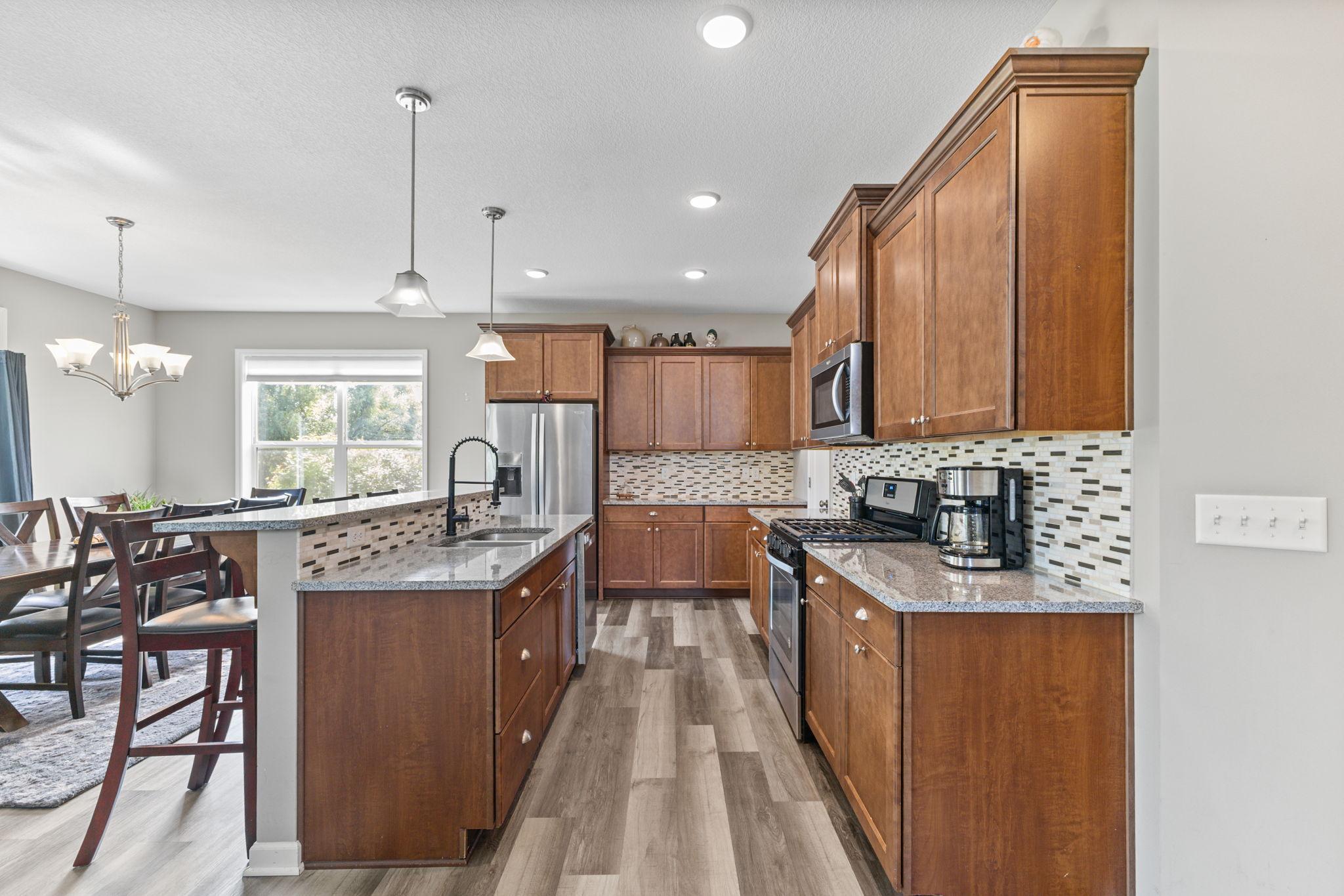 Kitchen features a large center island with seating, extensive cabinetry, and a clean tiled backsplash. Stainless steel appliances and durable surfaces make it both functional and easy to maintain, with a natural flow into the dining space.