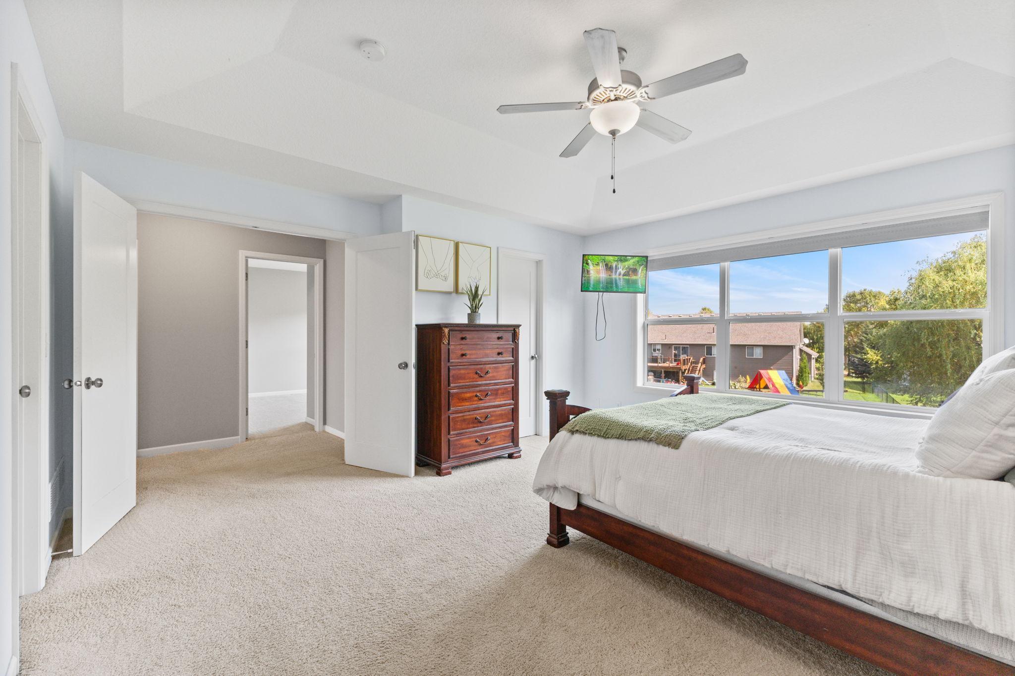 Spacious primary bedroom with a tray ceiling that adds height and dimension. East-facing windows overlook the backyard and bring in natural morning light, with plenty of room for a full bedroom setup and additional space to relax.