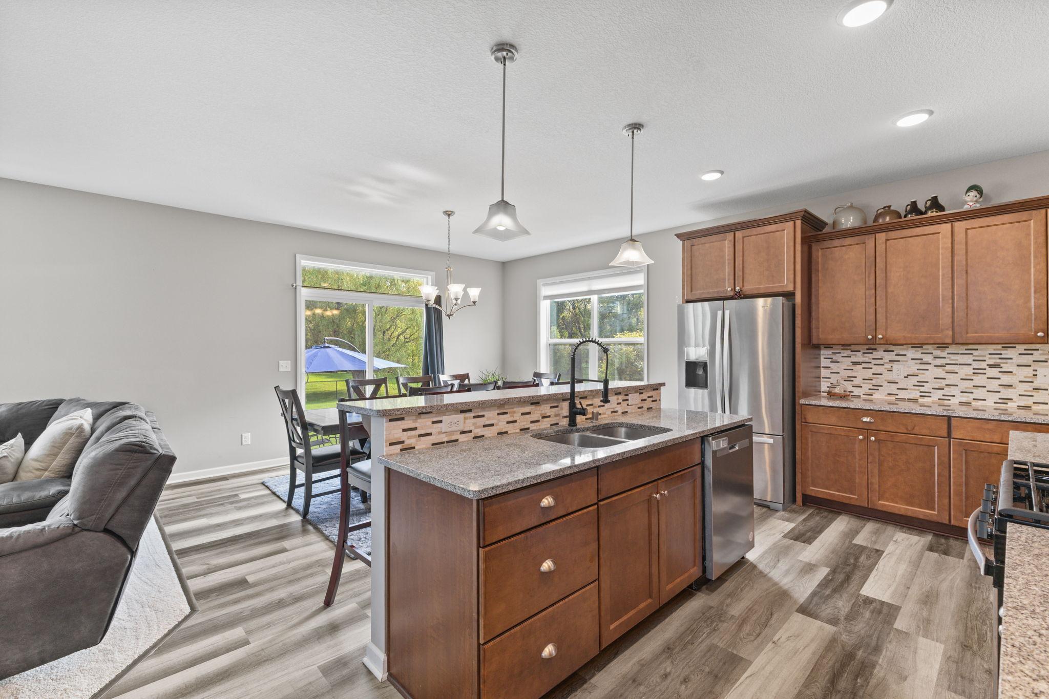Kitchen and dining area with new flooring, center island, and stainless steel appliances. East-facing windows bring in morning light and include custom blinds, with easy access to the backyard patio for indoor-outdoor flow.