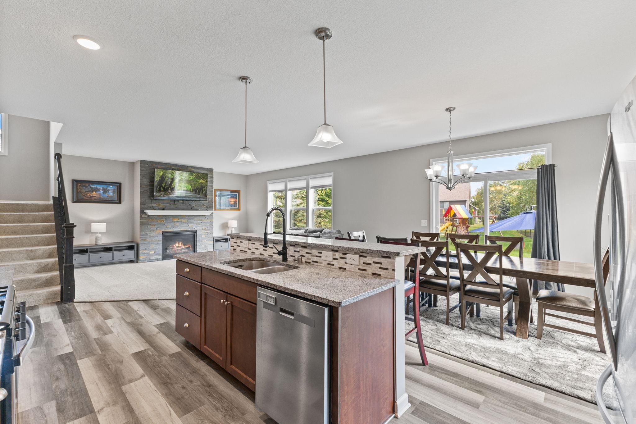 Open kitchen with center island and sink, flowing into the dining area with patio access and views of the backyard. Connected living room with a stone fireplace creates a functional layout for everyday living and entertaining.