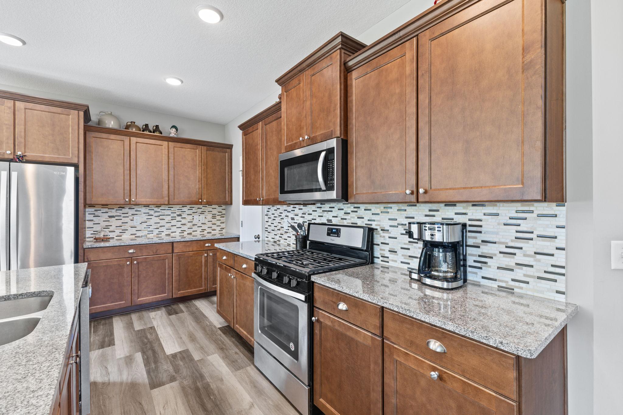 Extensive cabinetry and granite countertops provide ample prep and storage space, complemented by a tiled backsplash and stainless steel appliances. A large pantry just around the corner adds even more convenient storage.